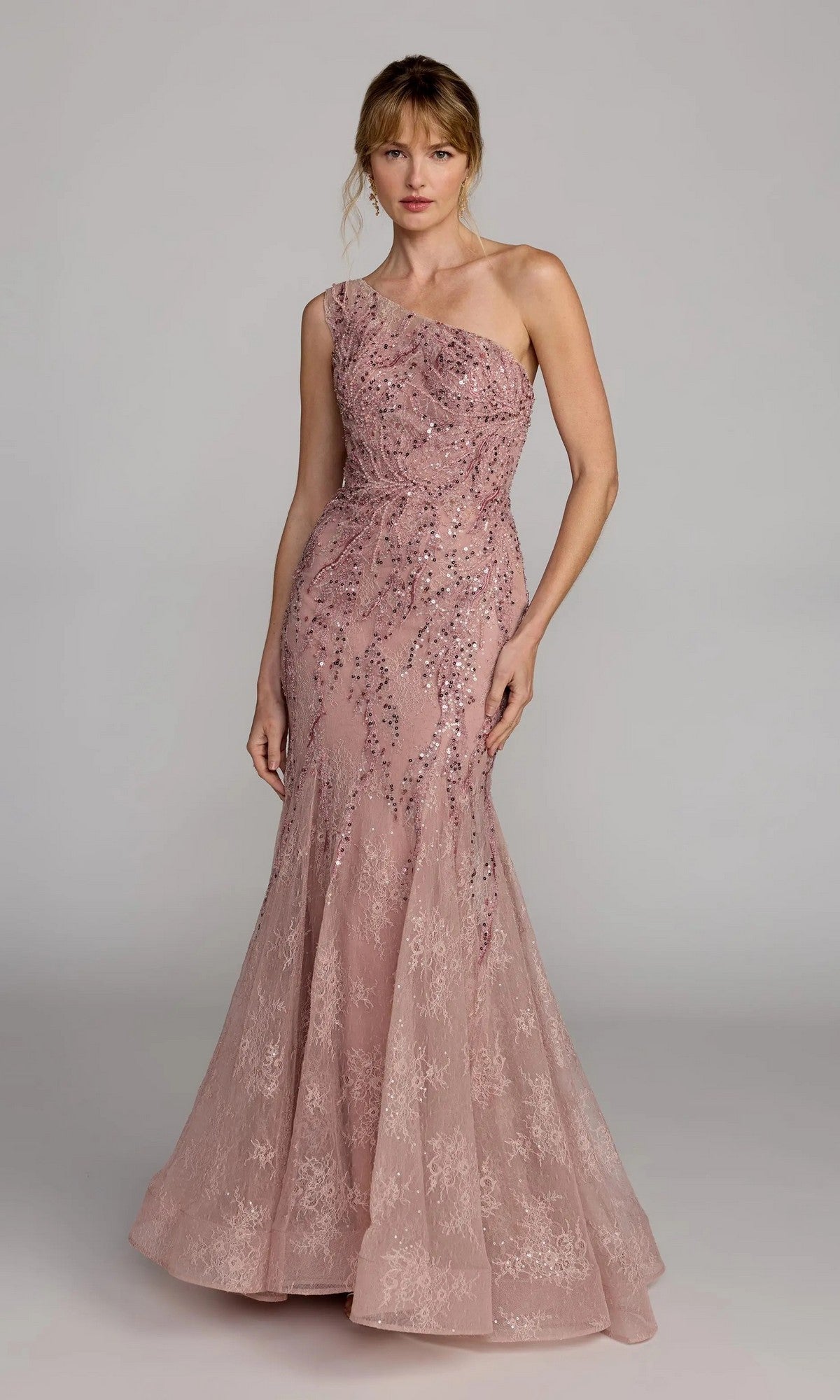 A woman wears the Mac Duggal 20482 long formal dress—a blush pink, one-shoulder mermaid gown with embellished lace and sequins—standing against a plain gray background.