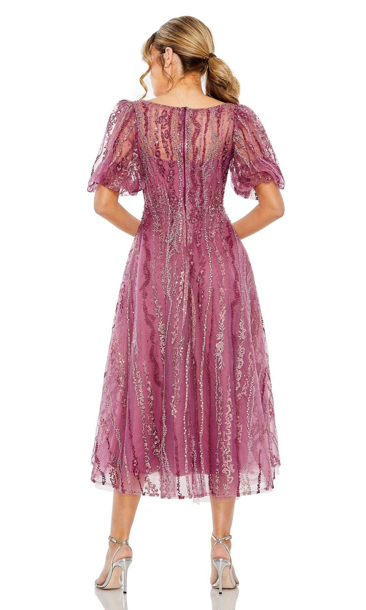 Woman facing away in the mauve Mac Duggal 20485, a knee-length embroidered wedding-guest dress featuring sheer short sleeves, sequin embellishments, and paired with silver high-heeled sandals.