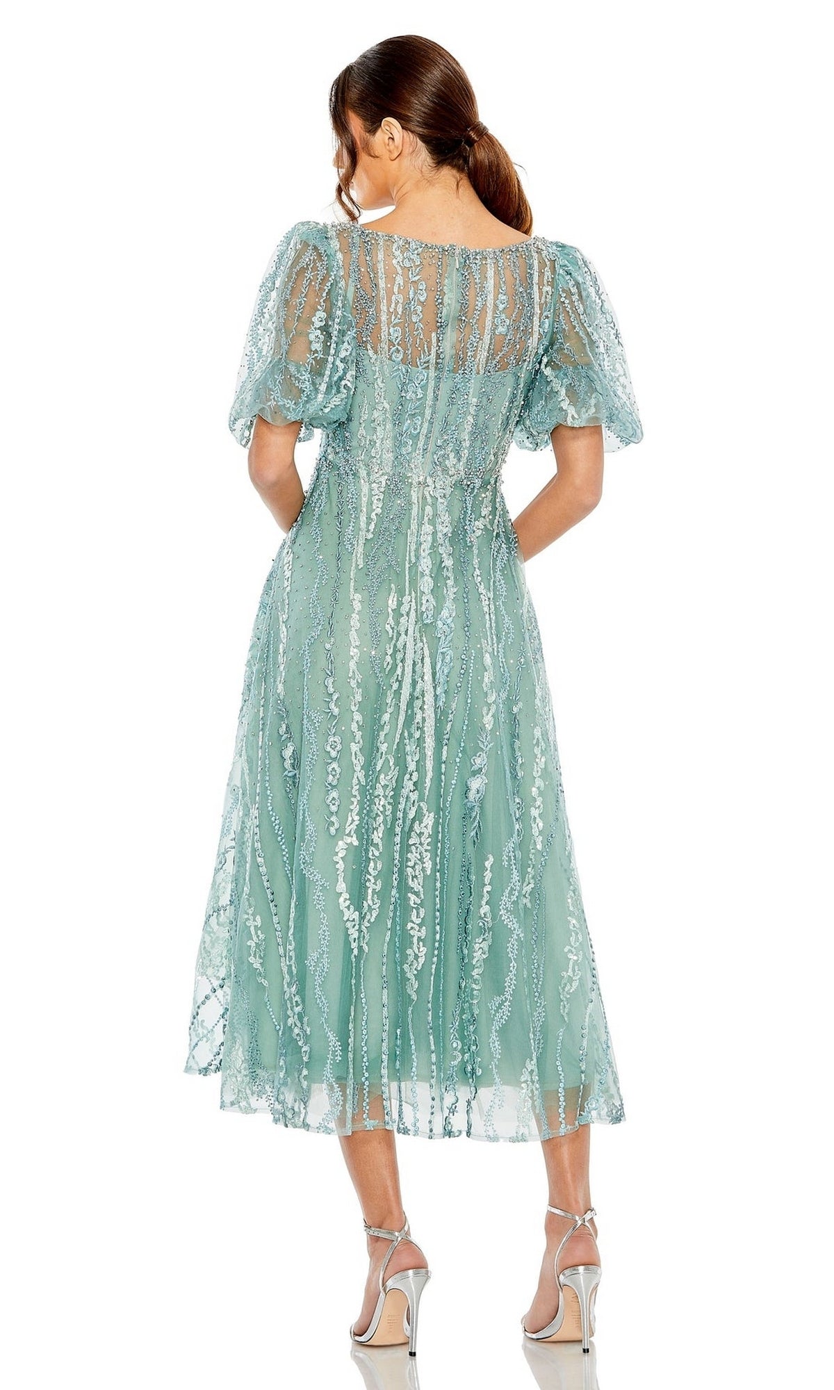 A woman faces away, wearing the Mac Duggal 20485 Embroidered Wedding-Guest Dress in light blue-green with short puff sleeves, paired with silver high-heeled sandals.