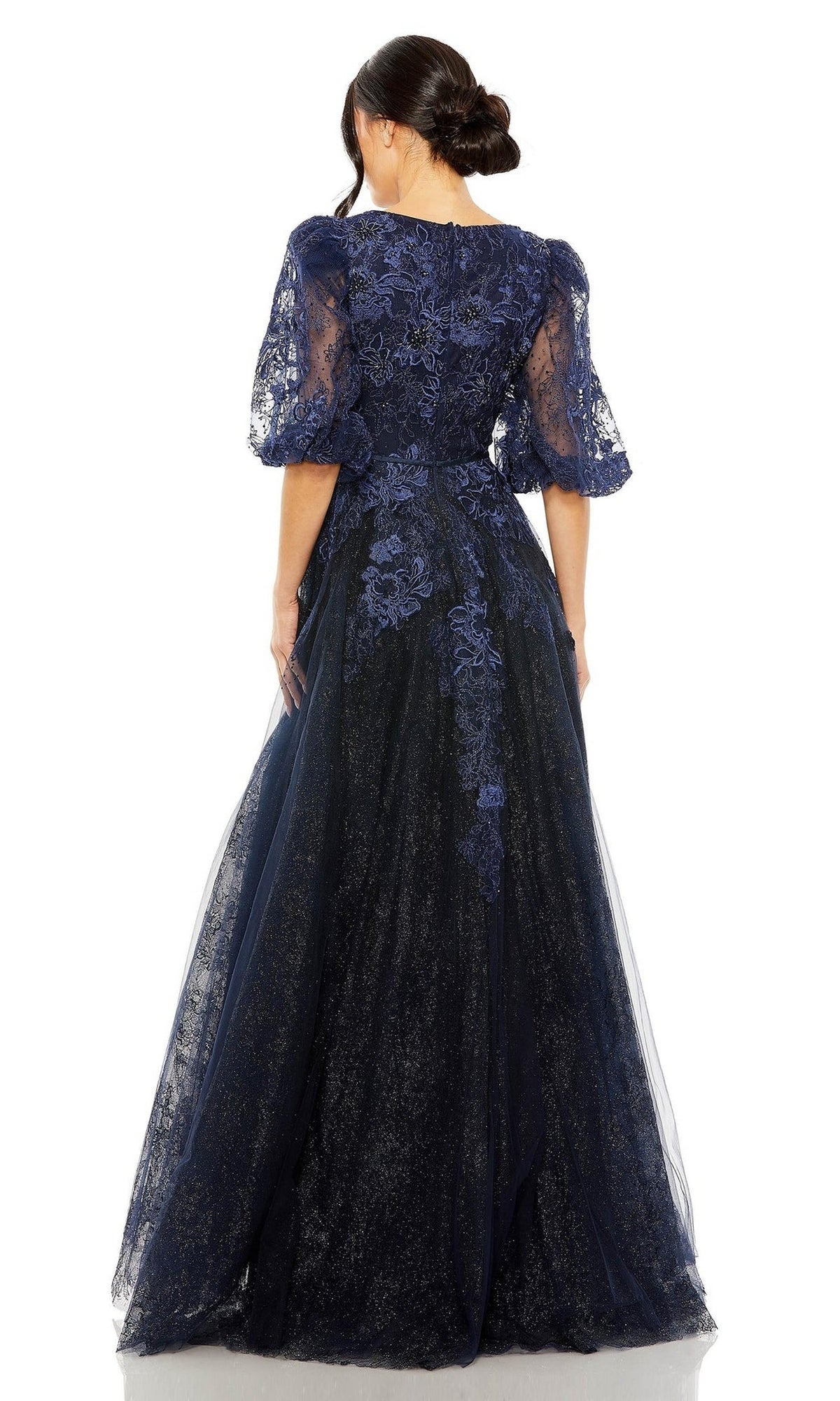 A woman is shown from the back against a white background wearing the Long Formal Dress 20506 by Mac Duggal, featuring midnight blue lace with sheer sleeves and floral embroidery in an elegant A-line silhouette.