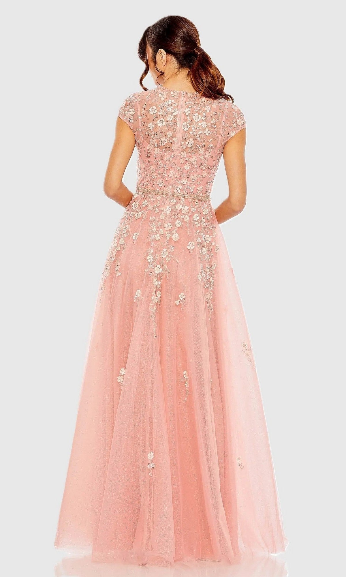 A woman stands with her back to the camera against a light gray background, wearing the Mac Duggal 20511—a floor-length, short-sleeved pink formal dress featuring floral embroidery.