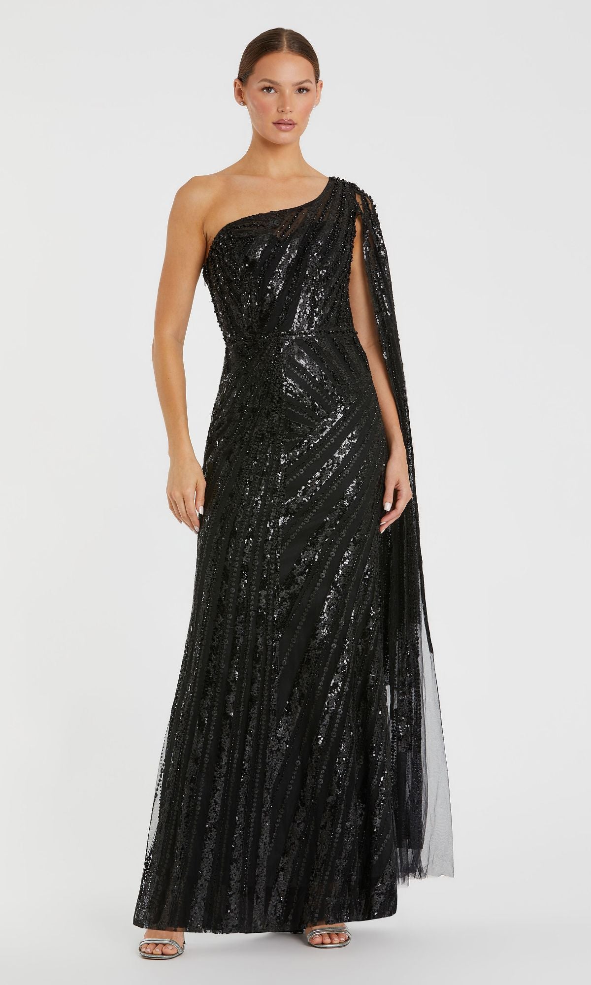 A woman models the Mac Duggal 20528 One-Shoulder Long Prom Gown—a floor-length black sequined dress with a draped cape—standing against a plain white background.