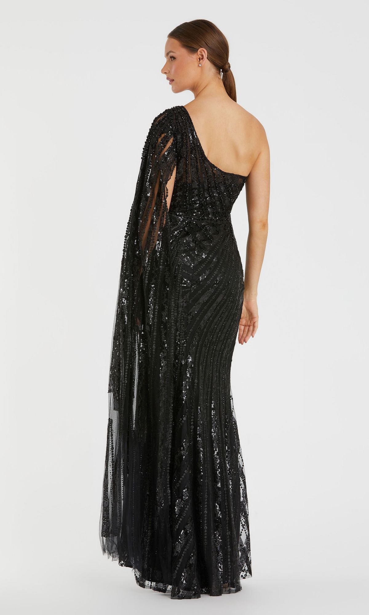 A woman models the Mac Duggal 20528 One-Shoulder Long Prom Gown—a floor-length black sequin dress with sheer draped detailing—standing against a plain white background.