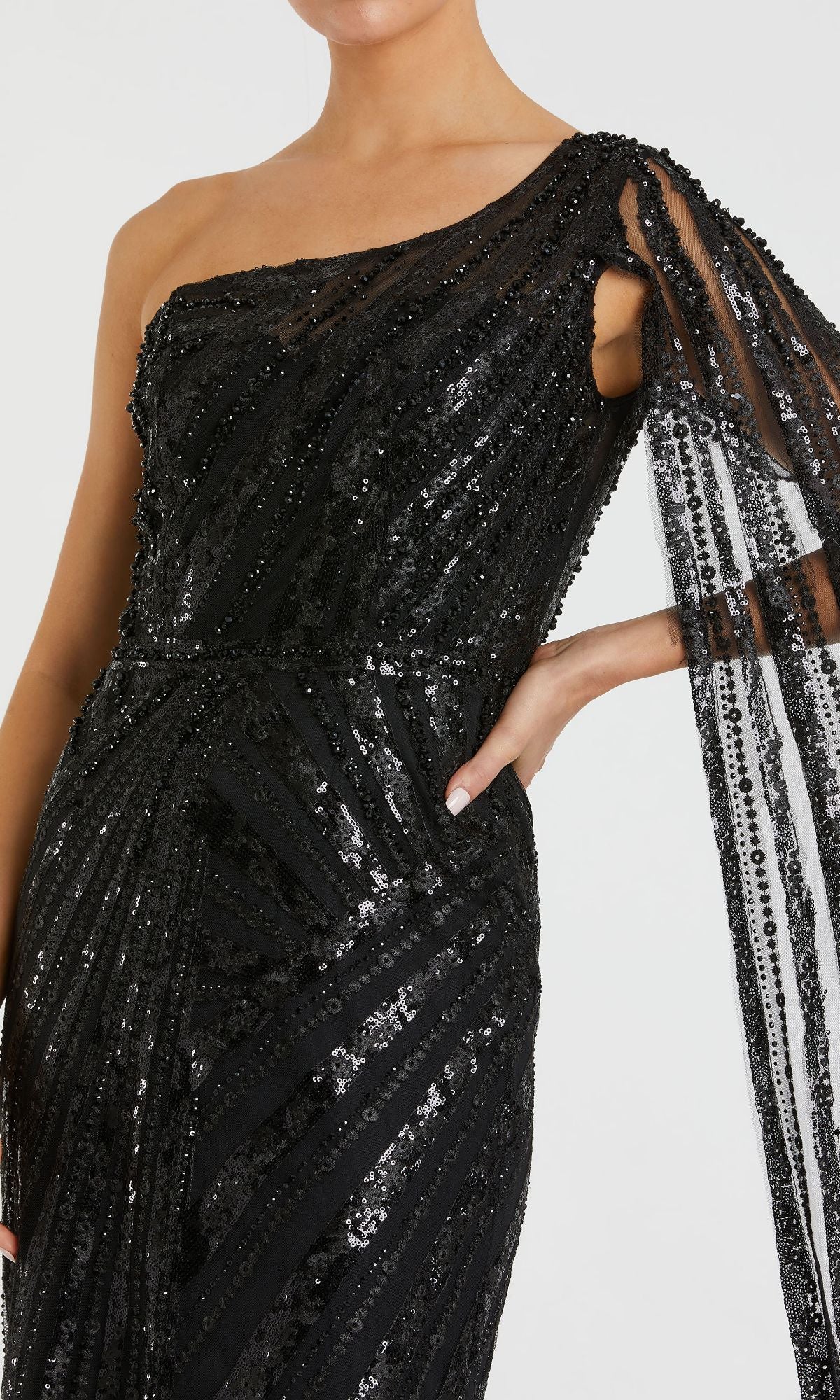 A person wears the Mac Duggal 20528, a black one-shoulder long prom gown featuring sequins and sheer, beaded draping on one arm.