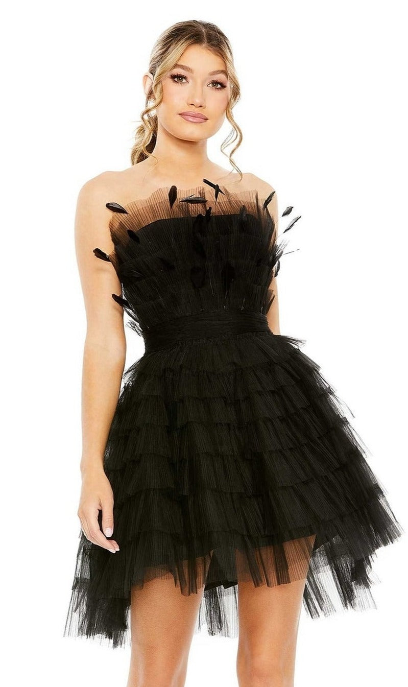 A woman in the Mac Duggal 20529 Strapless Ruffle Party Dress, featuring black tulle tiers and feather-like embellishments, stands against a plain white background.