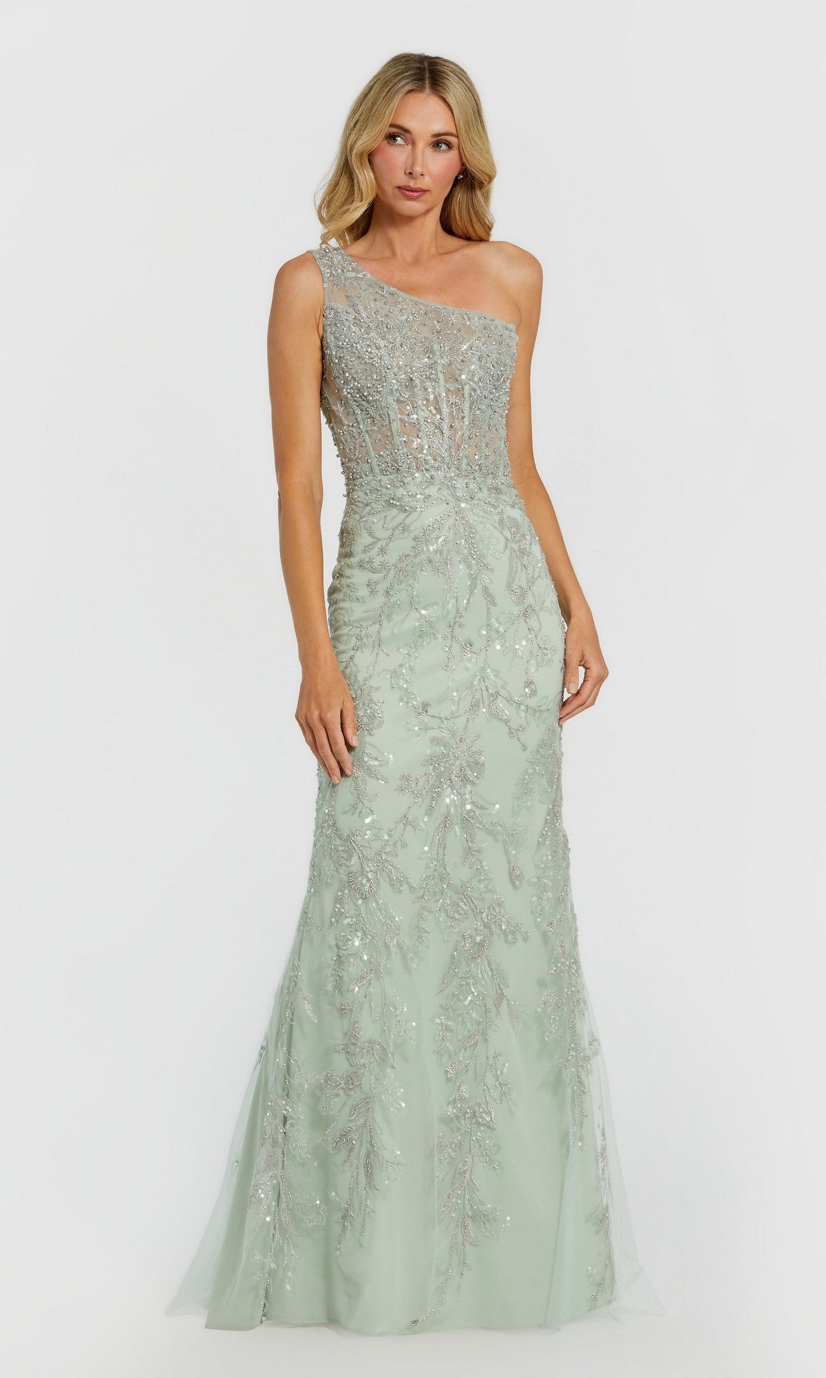 A woman in a sage Mac Duggal 20543 long formal dress featuring one shoulder and silver sequin embellishments stands against a plain background.