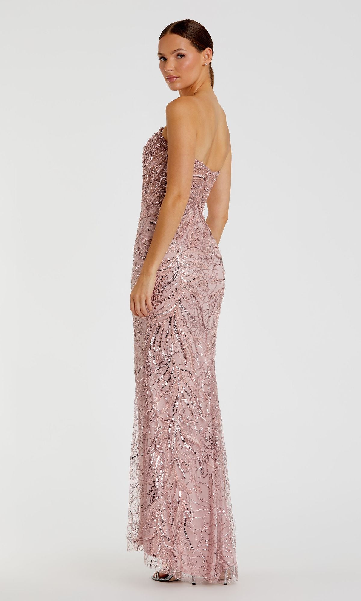 A woman poses gracefully in the Strapless Long Beaded Prom Dress by Mac Duggal (style 20544), a floor-length, light pink gown, looking over her shoulder against a plain white background.