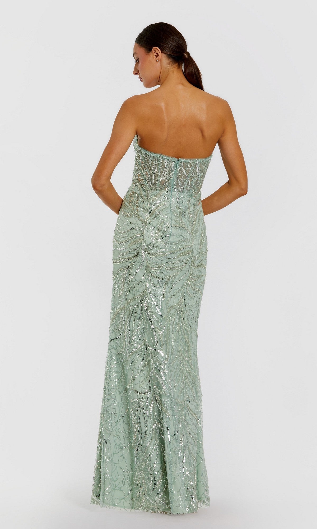 A woman faces away from the camera, wearing the Mac Duggal 20544 Strapless Long Beaded Prom Dress in light green, featuring sequins and intricate patterns.