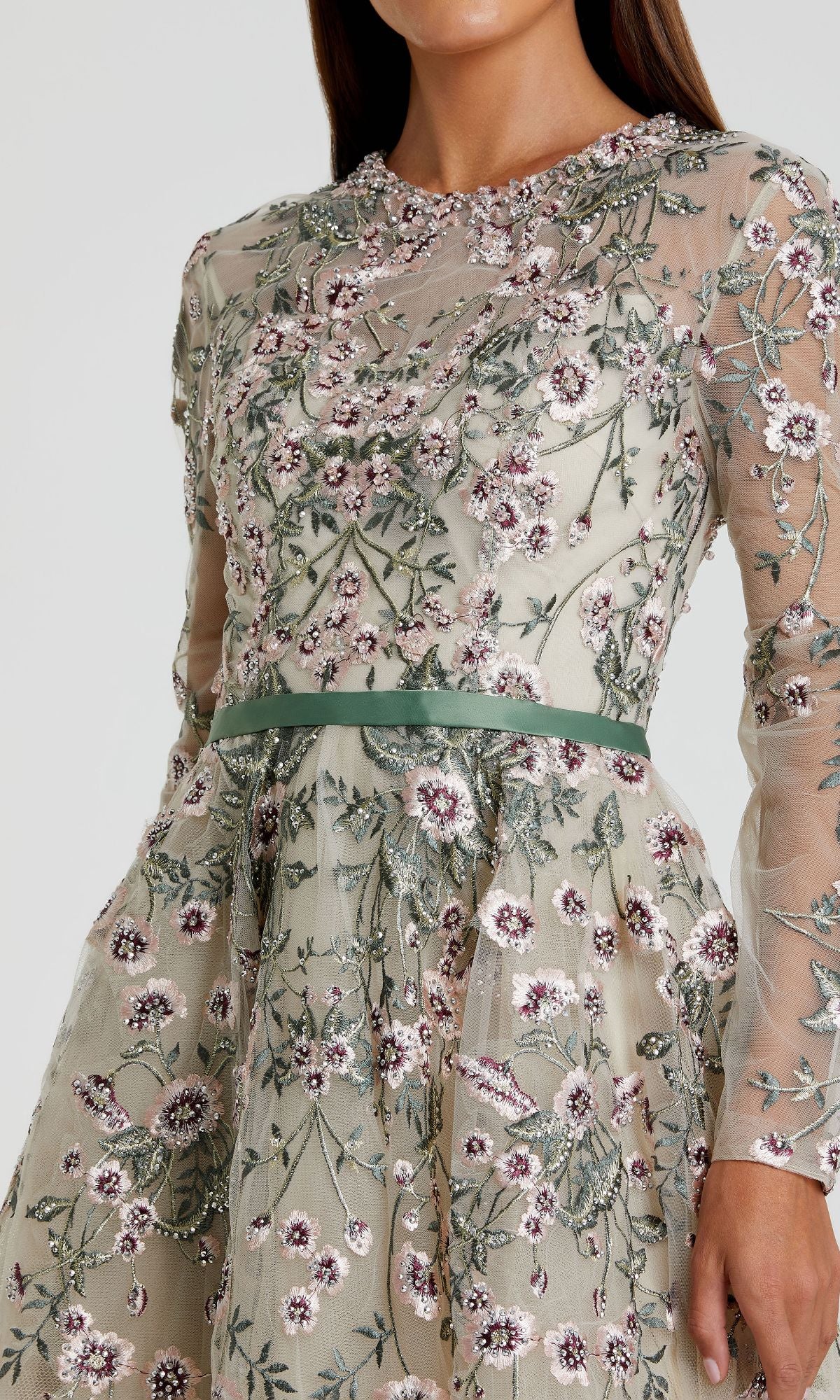 A woman models the Mac Duggal 20580 Sage Long Sleeve Formal Gown, showcasing its embroidered floral sheer sleeves and sage green satin waistband, pictured from shoulders to mid-thigh.