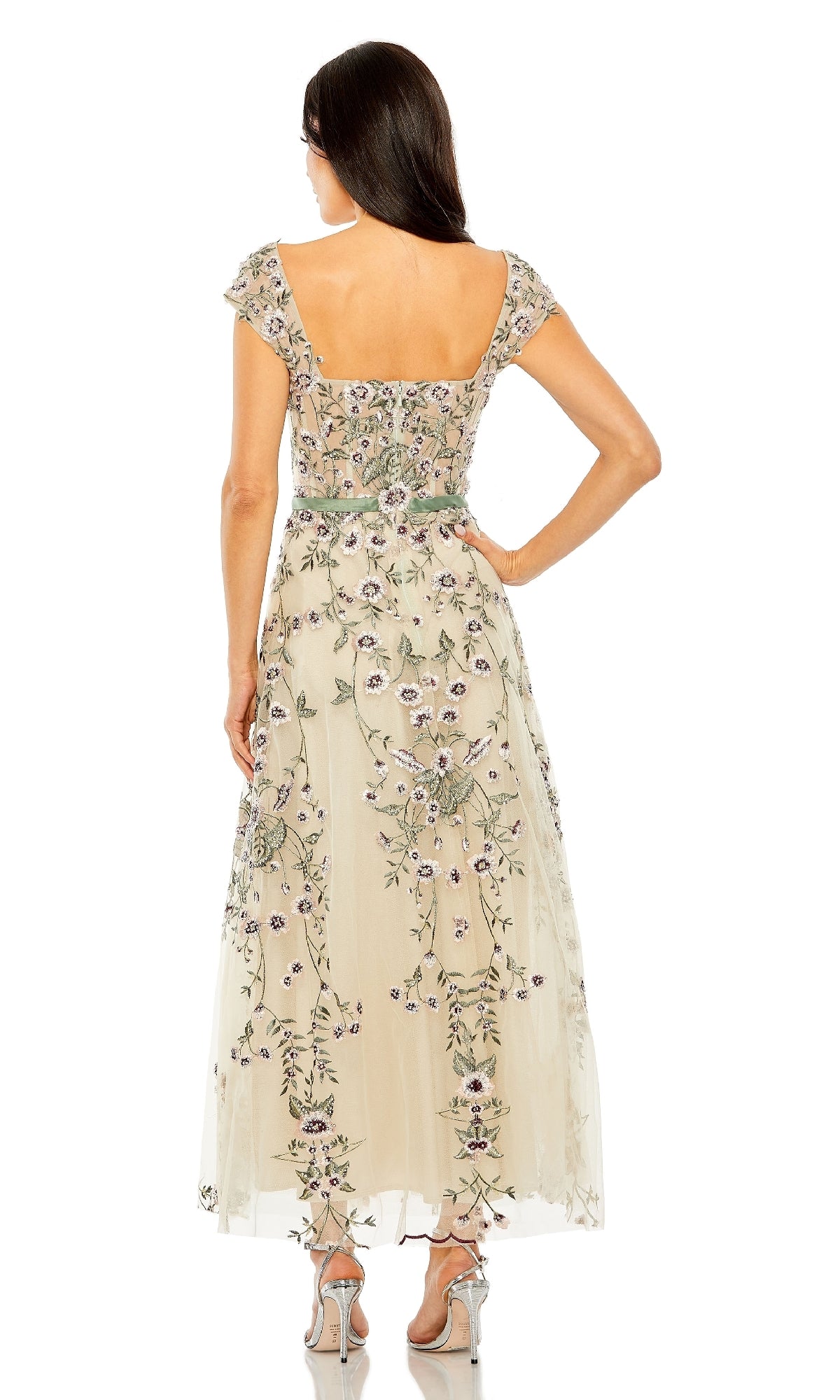 A woman faces away, wearing the Mac Duggal 20582 Cap-Sleeve Nude Midi Party Dress with floral embroidery and an open back, paired with silver high-heeled sandals.