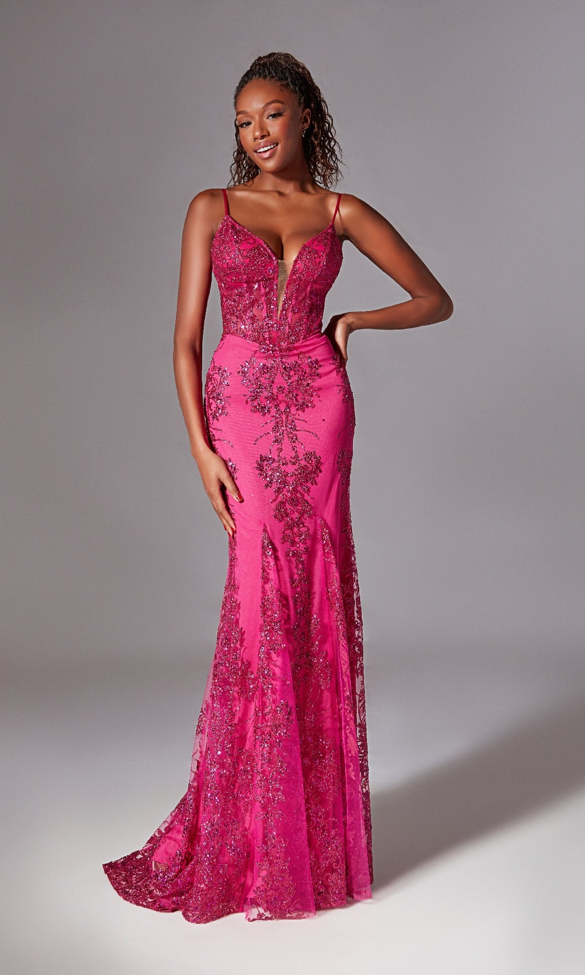 A woman smiles against a grey background wearing the Aerie Couture 206, a strappy-back, fitted pink floor-length prom dress with glitter print and intricate sequin details.