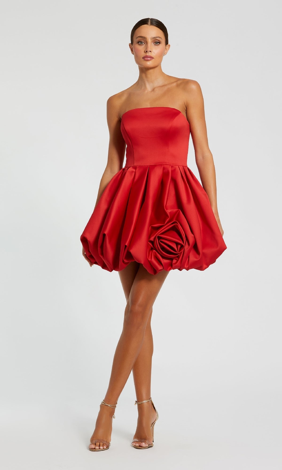 A woman wears the Mac Duggal 20705 Red Rose Bubble-Hem Hoco Dress—strapless, satin a-line with a rose detail—paired with silver high-heeled sandals.