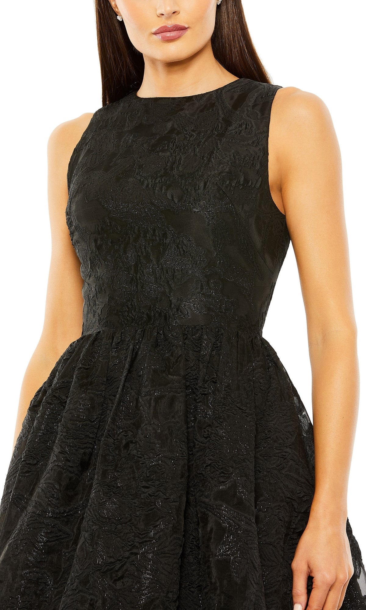 A woman wears the Brocade High-Low Formal Dress by Mac Duggal (20714), featuring a sleeveless design, textured black fabric, fitted bodice, and a flared high-low skirt.