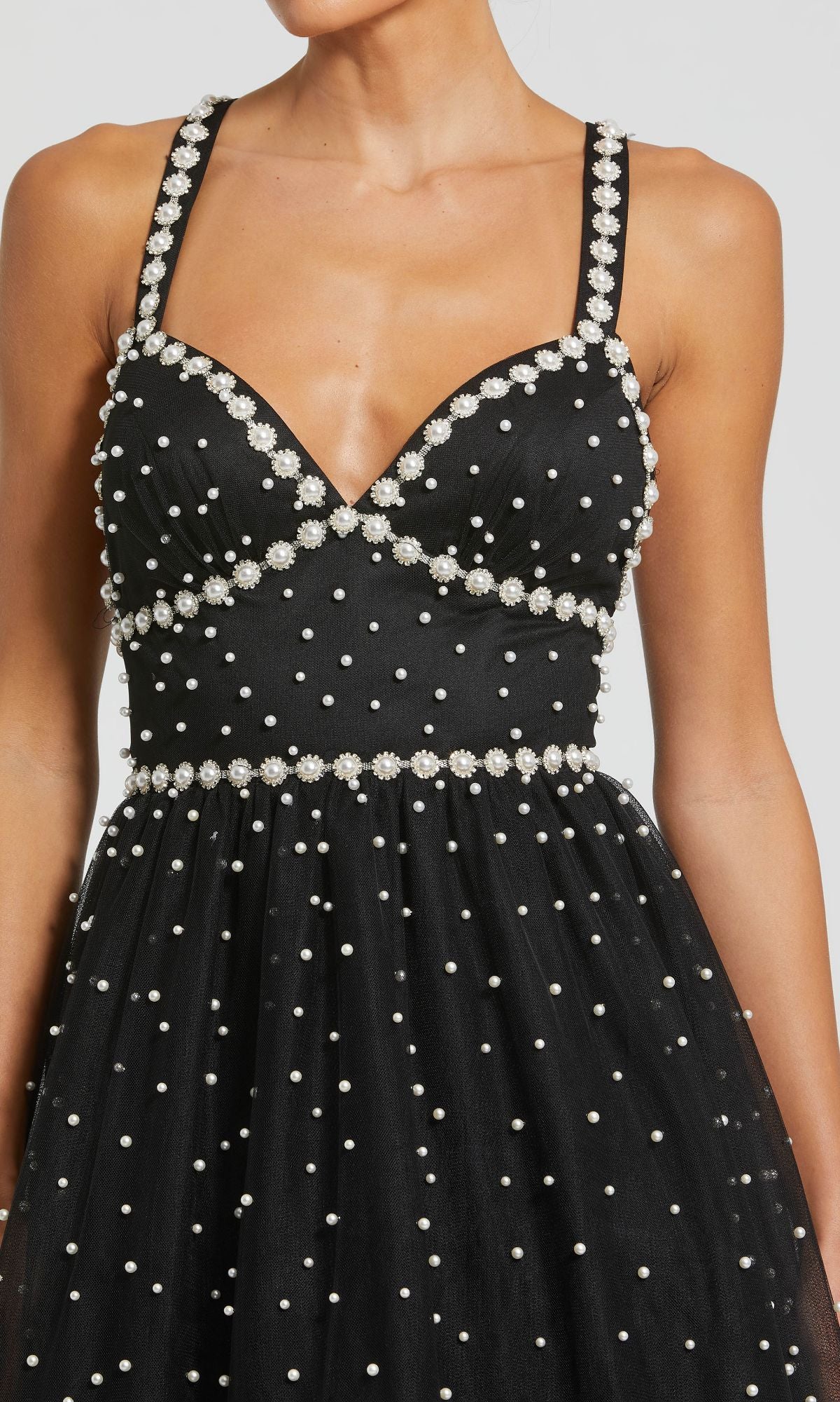 A woman wears the Mac Duggal 20747 Pearl High-Low Black Prom Dress, a sleeveless gown beautifully adorned with white pearls and floral accents on the straps, neckline, and waist.