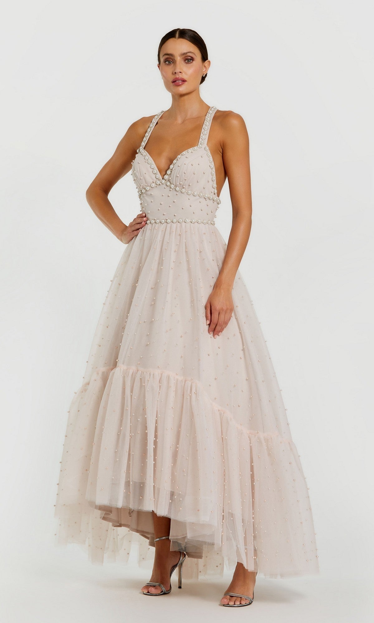 A woman stands against a plain white background in the Pearl High-Low Black Prom Dress by Mac Duggal 20747, a sleeveless gown featuring tulle and pearl embellishments that highlight its elegant, high-low design.