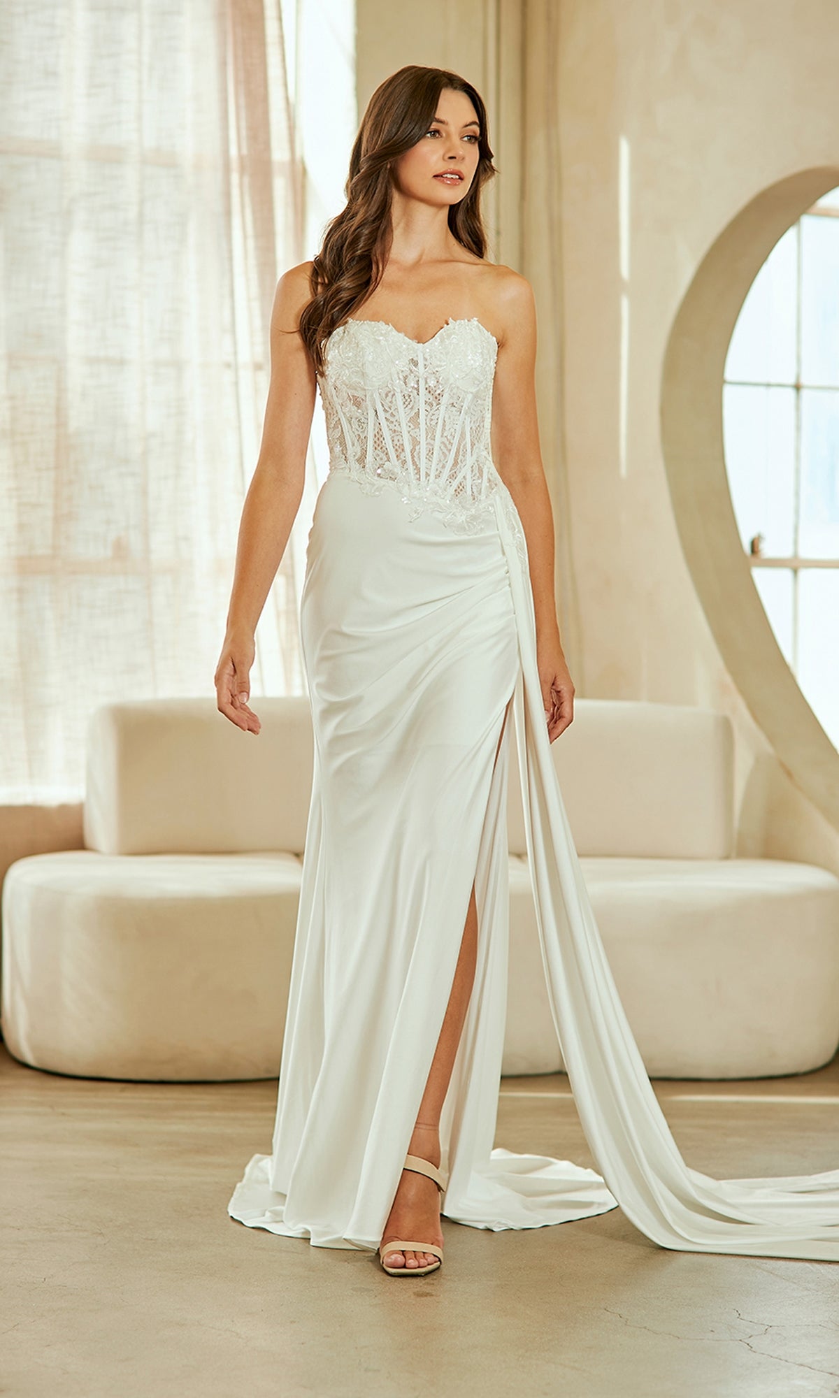 Woman wearing a white strapless gown with a slit in a softly lit room.