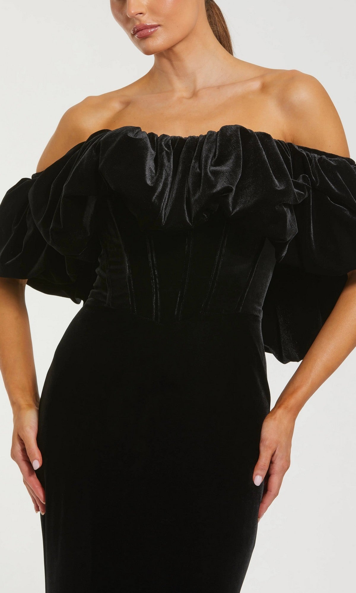 A woman wears the Mac Duggal 20766 long formal dress, an off-the-shoulder black velvet evening gown with a ruffled neckline and fitted bodice.