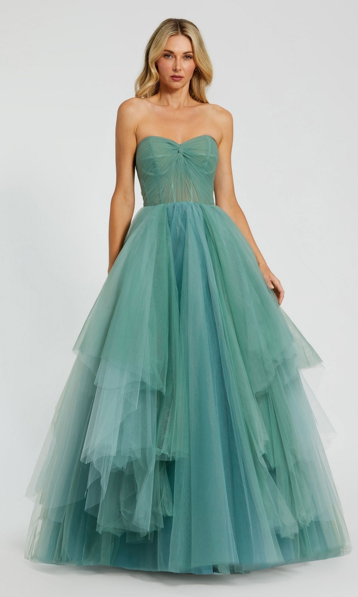 A woman stands against a plain light background wearing the Long Formal Dress 20772 by Mac Duggal, a strapless teal tulle ball gown with a ruched bodice, layered skirt, and classic floor-length elegance.