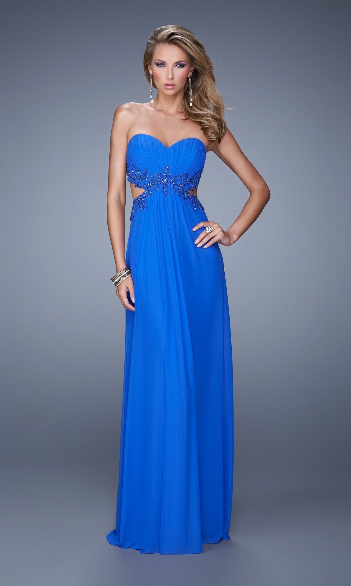 A woman models the La Femme Jersey Prom Dress 20826—strapless, royal blue, floor-length with side cutouts and beaded lace—against a gray background.