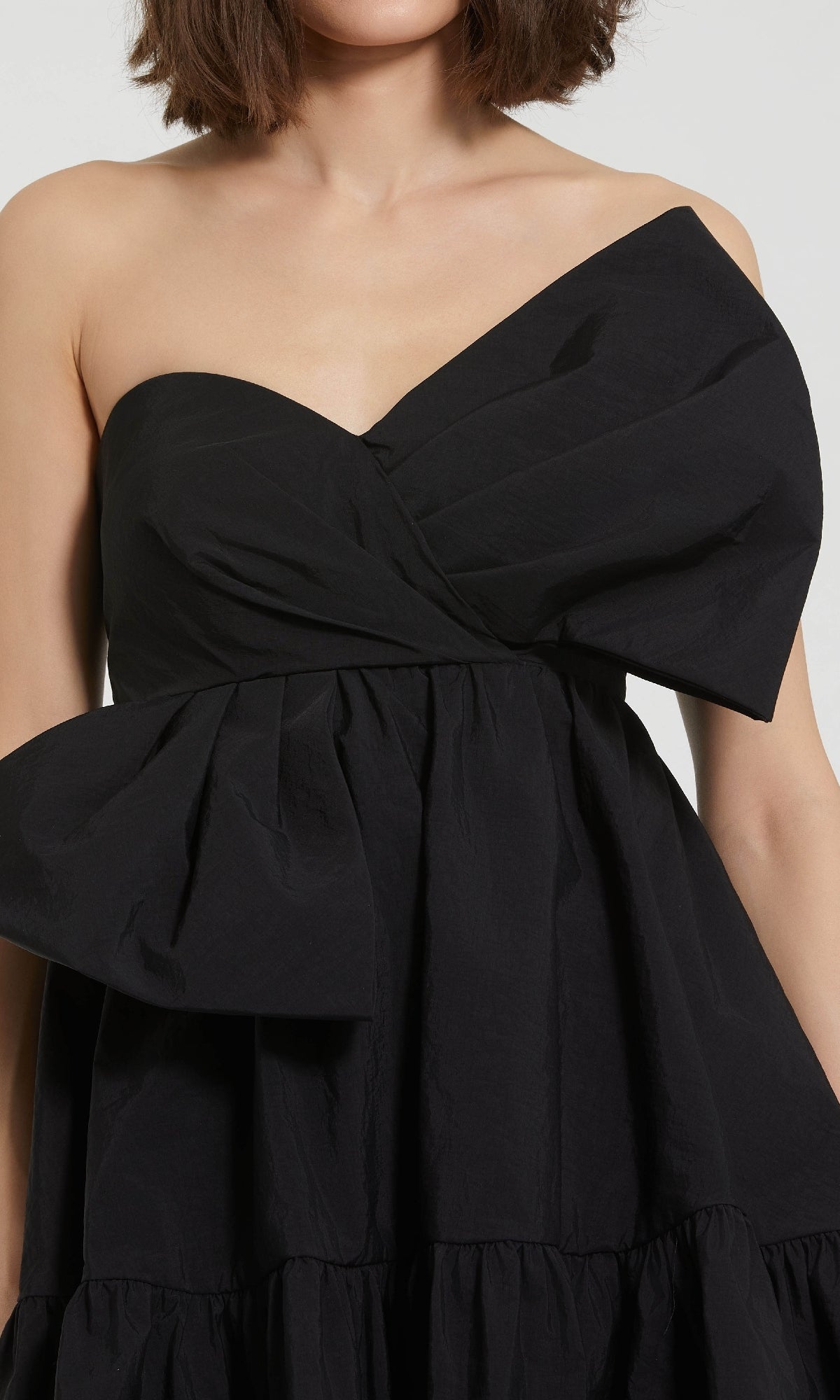 A person wearing the Mac Duggal 20937 Strapless Short Bow Party Dress, a black asymmetrical design with a large bow on the bodice.