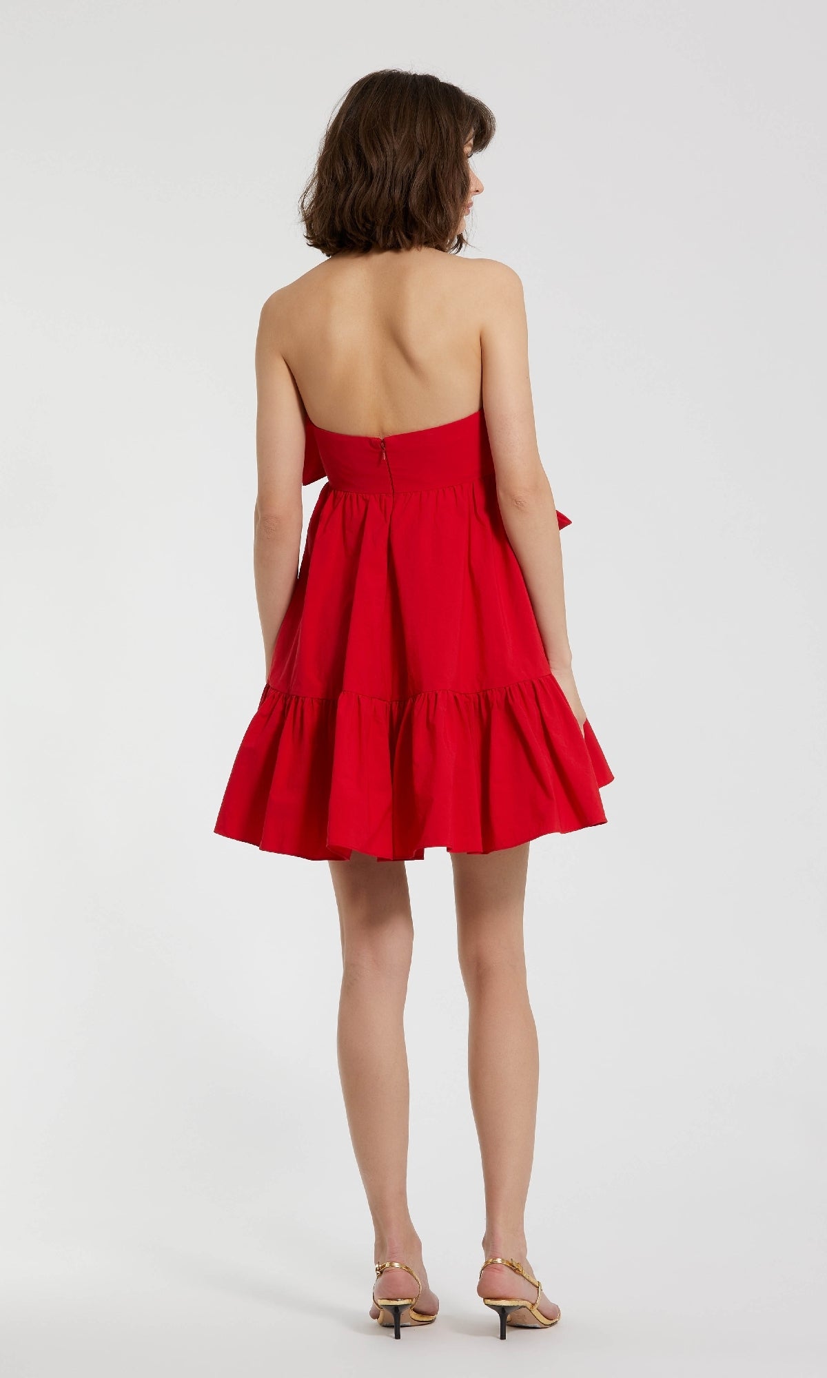 A woman wearing the Mac Duggal 20937 Strapless Short Bow Party Dress stands facing away from the camera against a plain white background.