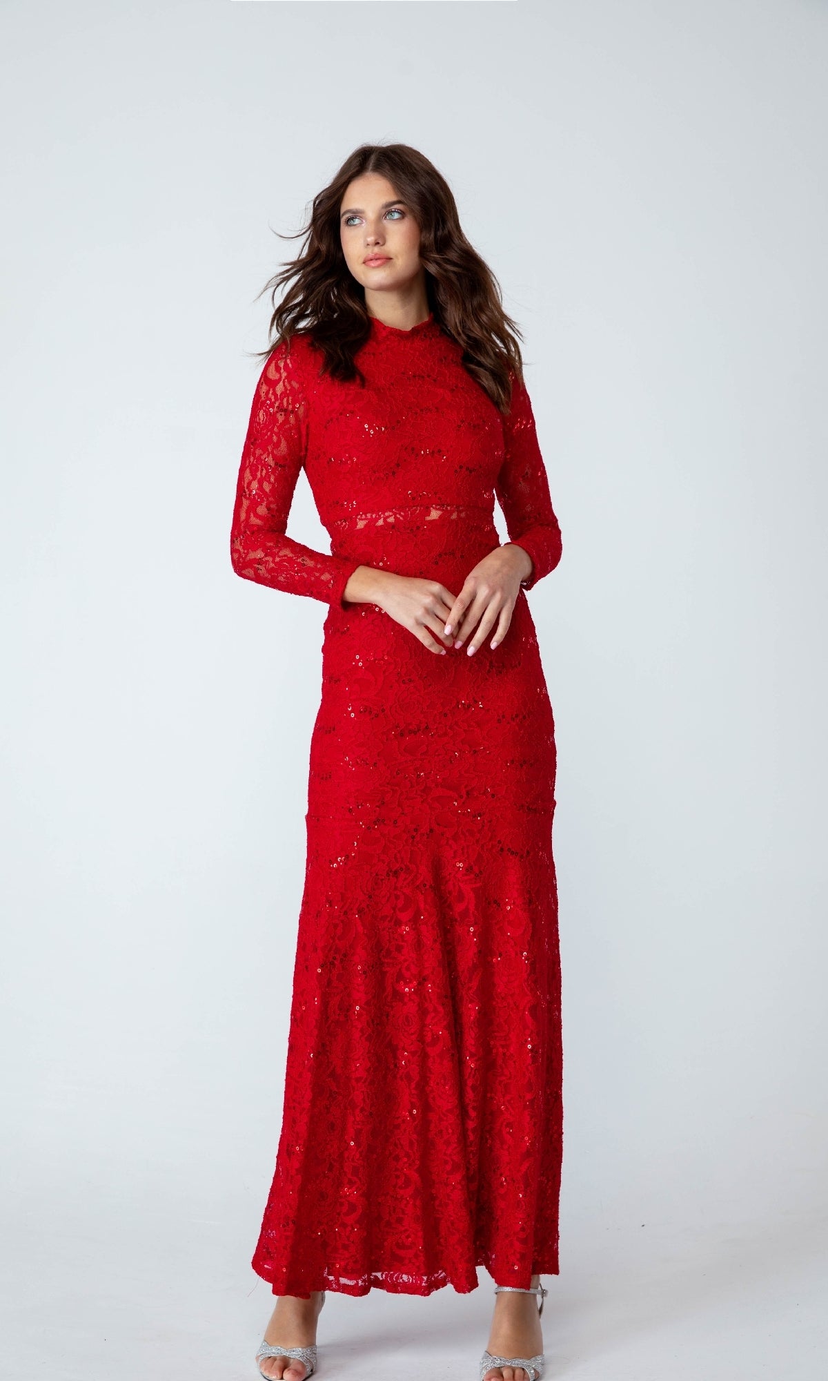 A woman poses against a plain white background wearing the Eureka 2095, a long-sleeve, floor-length red sequin-lace formal dress.