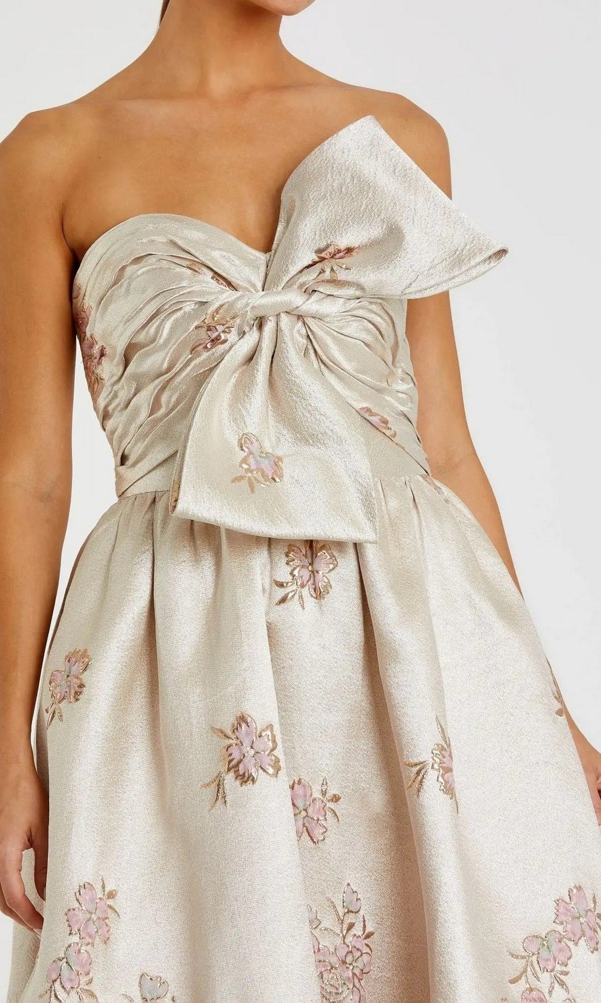 A woman wears the Mac Duggal 20974 long formal dress—a strapless ballgown featuring a large bow at the bust and delicate floral embroidery on the bodice and skirt.
