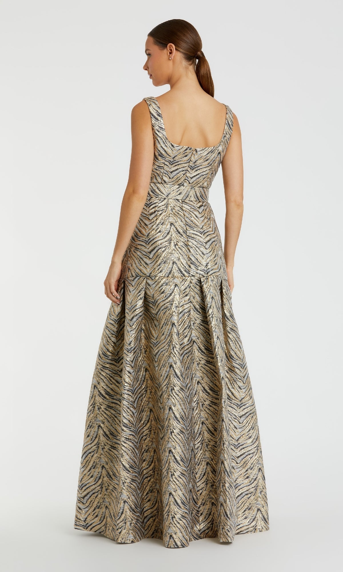 A woman stands facing away, wearing the Mac Duggal 21054 Gold Zebra-Print Long Prom Gown featuring a metallic pattern and pleated skirt.
