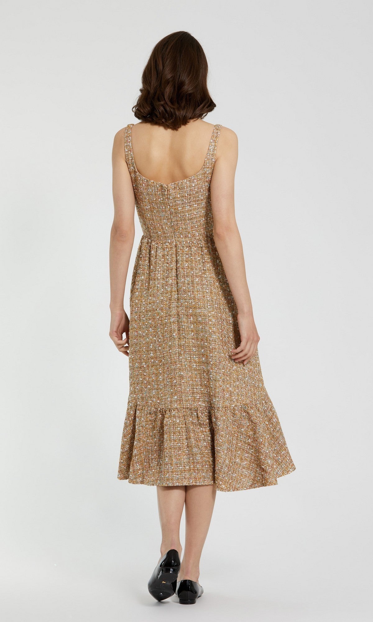 A woman faces away, wearing the Mac Duggal 21071 Boucle A-Line Midi Dress featuring a ruffled hem and square neckline in patterned boucle, paired with black shoes, set against a plain light background.