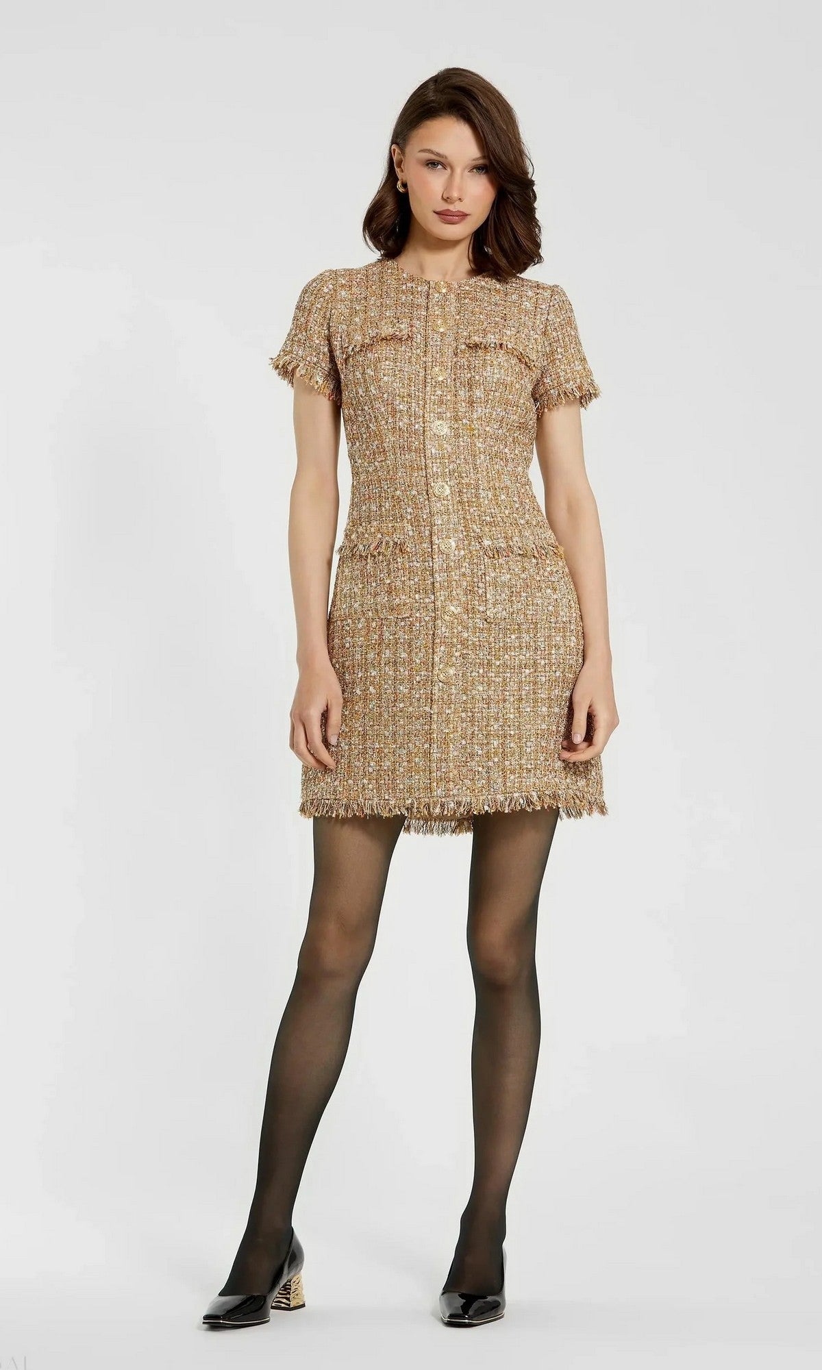 A woman stands facing forward in the Mac Duggal 21072 Short Wedding Guest Dress in Latte Multi, paired with black sheer tights and heels, against a plain light background.