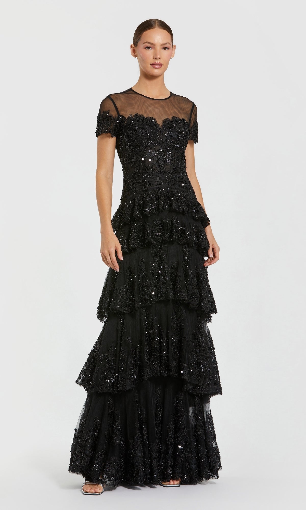 Woman wearing a black lace evening gown with tiered layers, standing in front of a white background