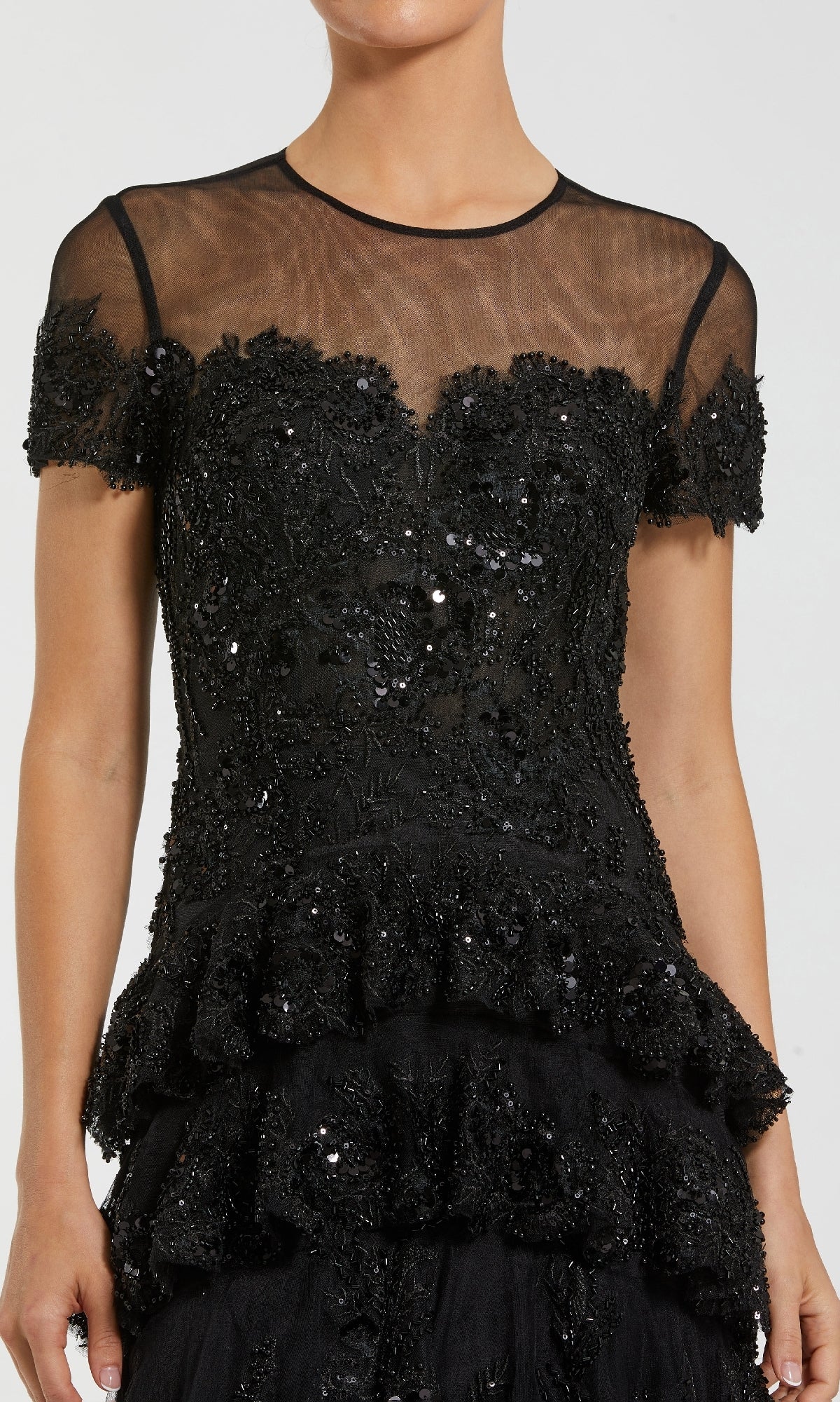 Woman wearing a black embellished evening gown standing in front of a white background