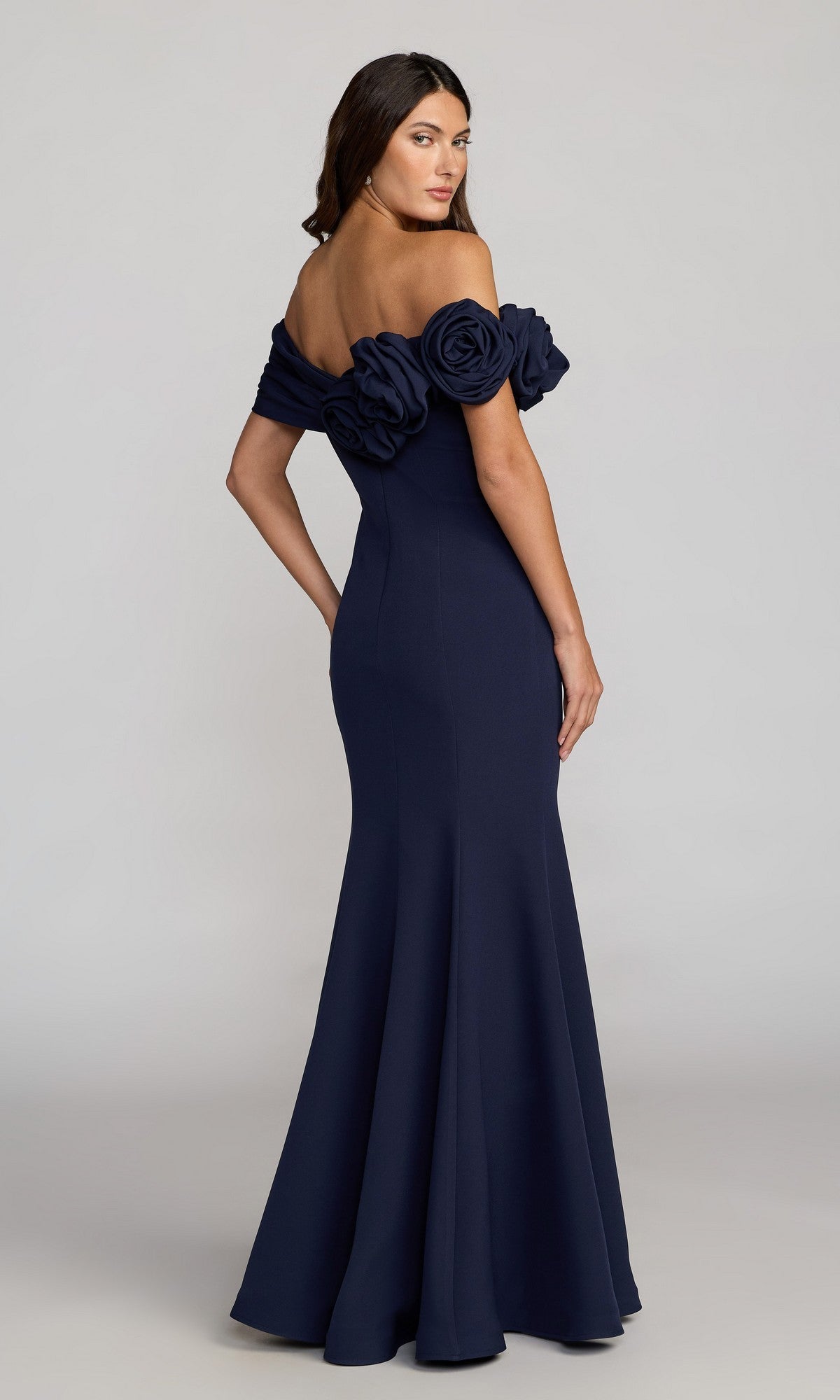 A woman poses against a plain light background in the Mac Duggal 21104 Off-Shoulder Long Formal Dress, a floor-length navy gown with mermaid silhouette and large floral sleeve accents.