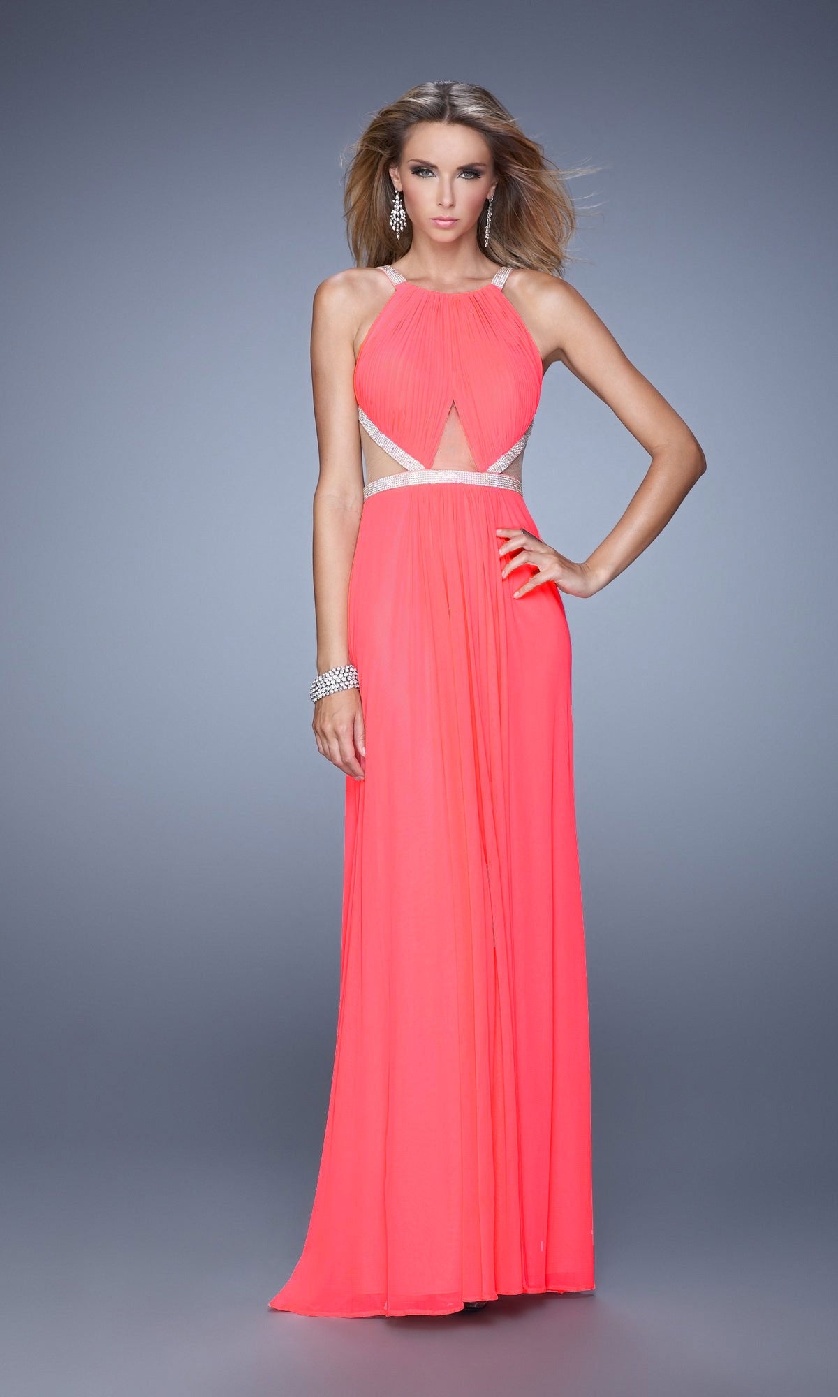 A woman poses against a plain gray background wearing the Long A-Line Prom Dress: La Femme 21145, a sleeveless coral gown with a halter neckline, cutouts at the waist and chest, and silver beaded accents.