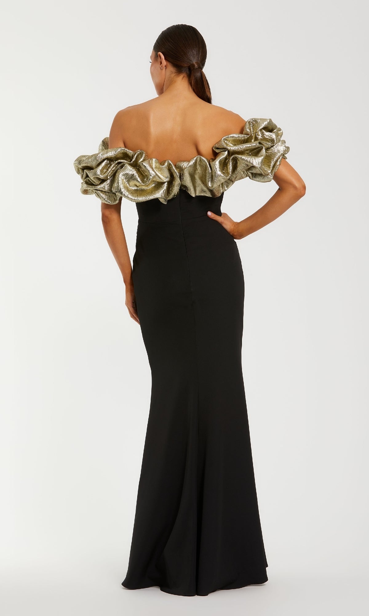 Woman showing the back of a black evening gown with gold ruffled off-the-shoulder straps standing in front of a white background.