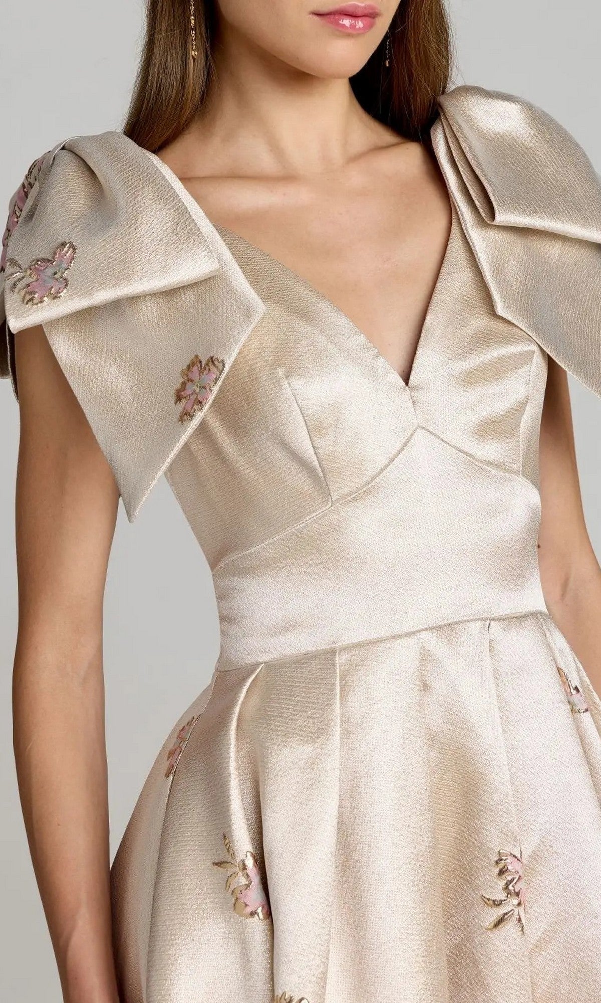 Model wearing the Mac Duggal 21204 long formal dress in beige satin brocade, featuring wide pleated shoulders and delicate floral embroidery, shown from shoulders to waist against a plain background and evoking the elegance of a ballgown silhouette.