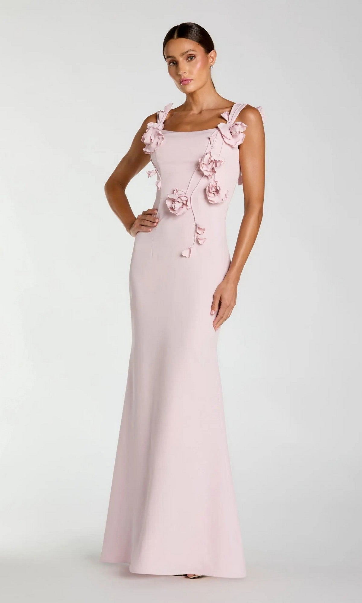 A woman wearing the Long Formal Dress: Mac Duggal 21236 in blush, featuring a floor-length silhouette with floral appliqués on the bodice, stands against a plain light background.