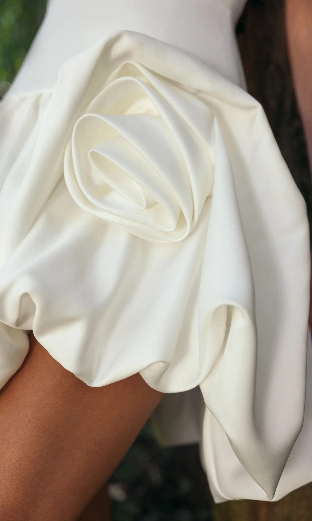 Close-up of the Mac Duggal 21237 short party dress in white satin, featuring fabric elegantly folded into a large rose shape, as worn by someone standing outdoors.