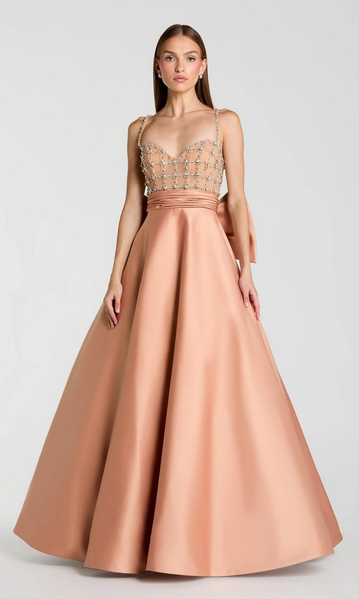 A woman wearing the Long Formal Dress: Mac Duggal 21242, a sleeveless dusty rose satin ballgown featuring a beaded sheer bodice and a full skirt, stands against a plain light background.