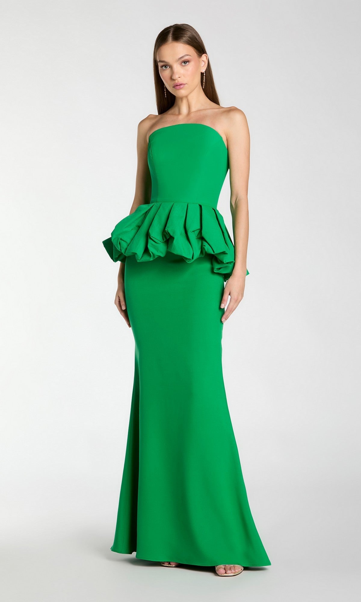 A woman stands against a plain background wearing the Mac Duggal 21243, a long formal dress in spring green featuring a strapless neckline, structured ruffle detail at the waist, and a subtle trumpet silhouette.