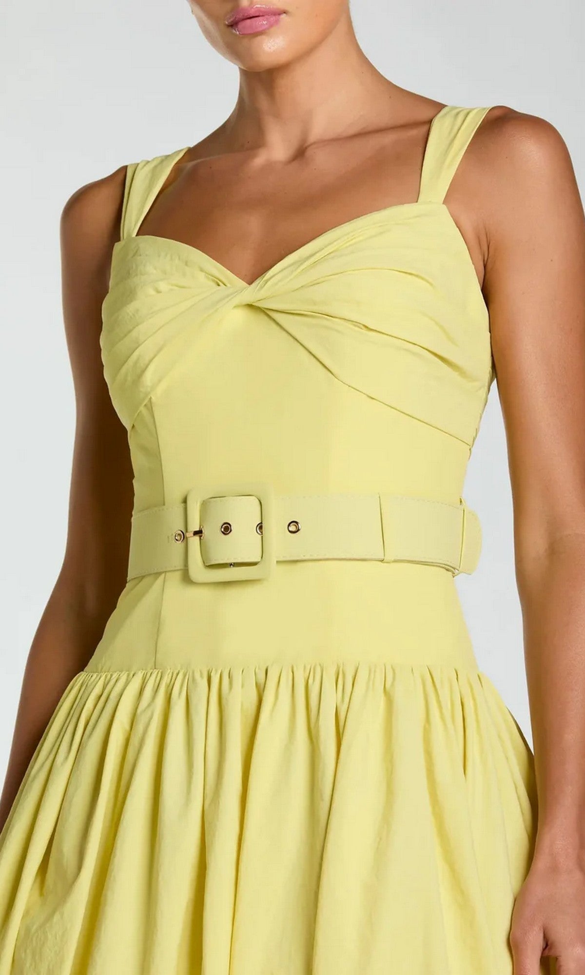A woman wearing the Mac Duggal 21251—a tea-length party dress featuring a sleeveless, light yellow design with a sweetheart neckline, gathered bodice, wide belt, and a full pleated skirt.