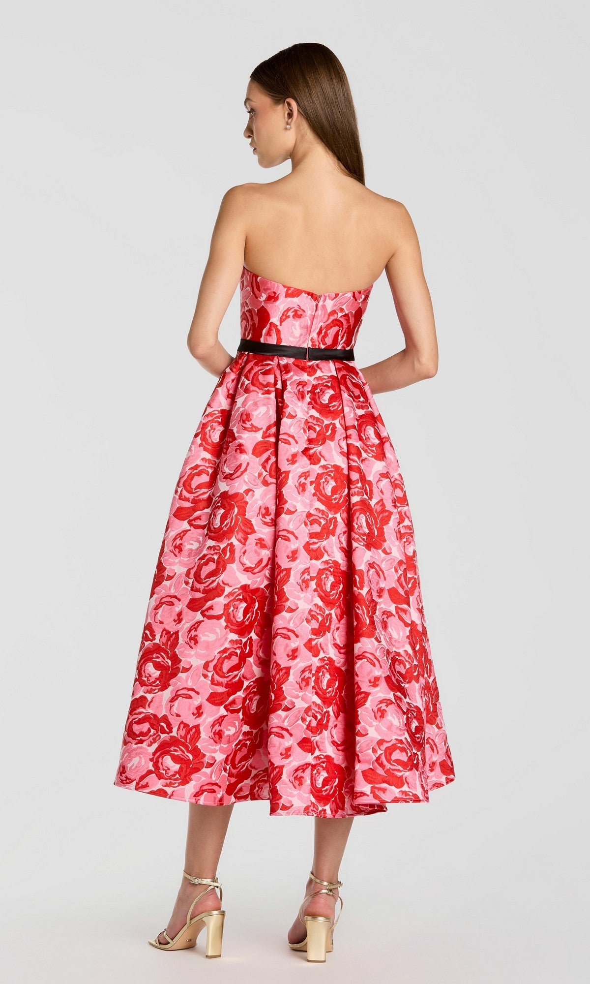 A woman faces away, wearing the Mac Duggal 21252 Tea-Length Party Dress—a strapless red party dress featuring a mid-length silhouette and red floral pattern—paired with metallic heels, standing against a plain background.