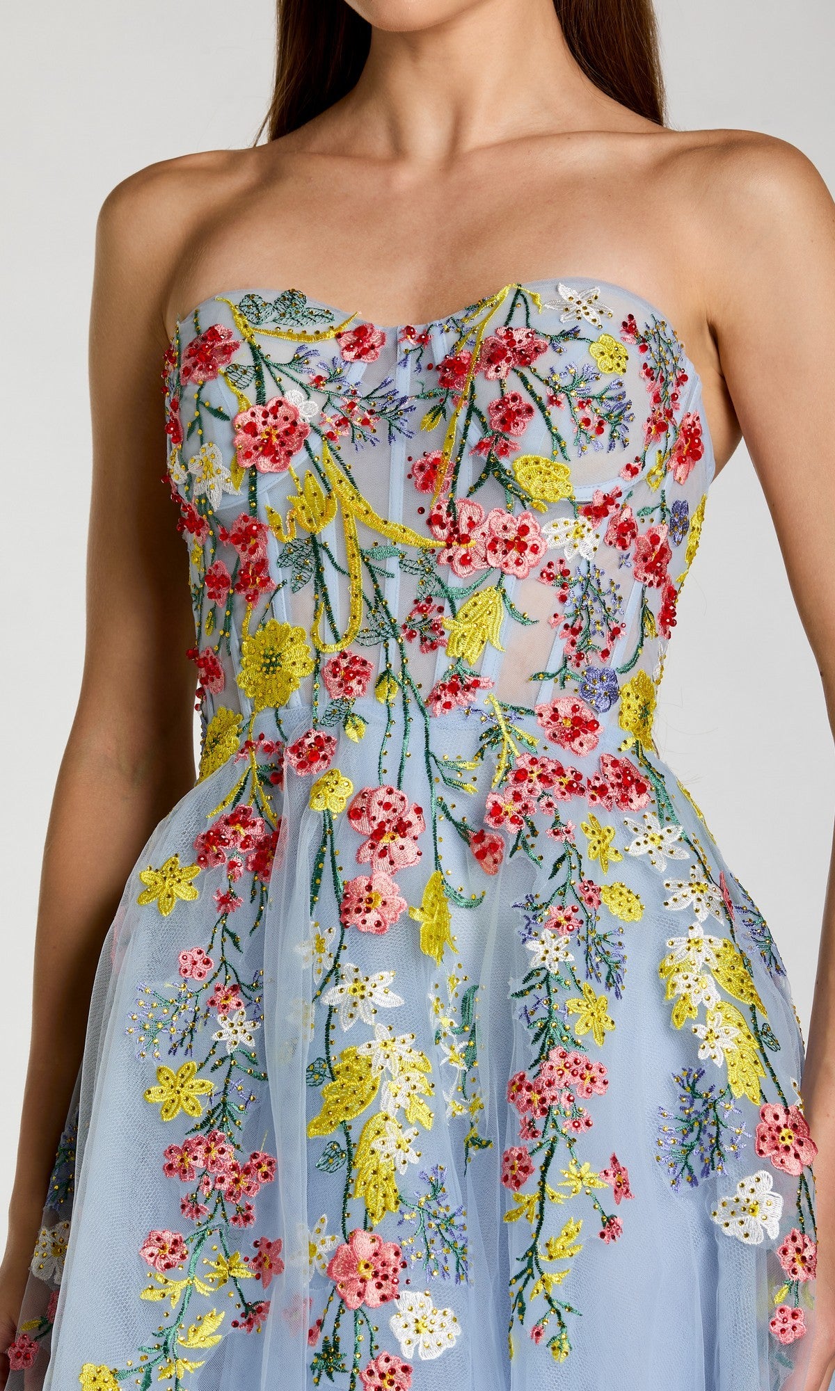 A woman wears the Tea-Length Party Dress: Mac Duggal 21304, a strapless blue party dress crafted in sheer tulle and adorned with colorful floral embroidery in red, yellow, and green. This gorgeous tea-length dress beautifully highlights the intricate floral details for an unforgettable statement look.