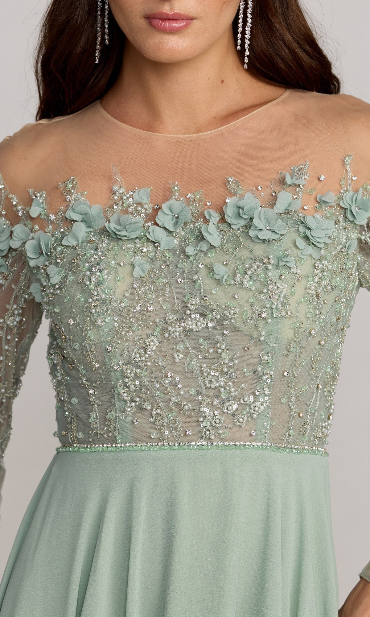 A woman is seen from the upper body wearing the Mac Duggal 21315 long formal dress in sage green, featuring a sheer neckline, floral appliqués, bead embellishments, and long sleeves.