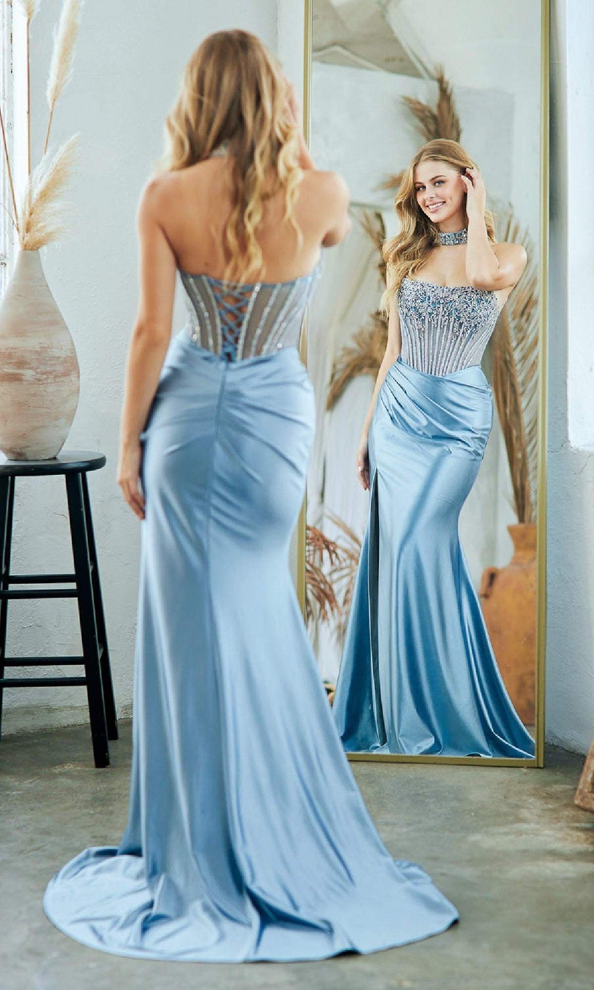 A woman in a strapless, fitted blue Long Sparkly Satin Prom Dress by Amelia Couture 2131 stands smiling at her reflection in the mirror.