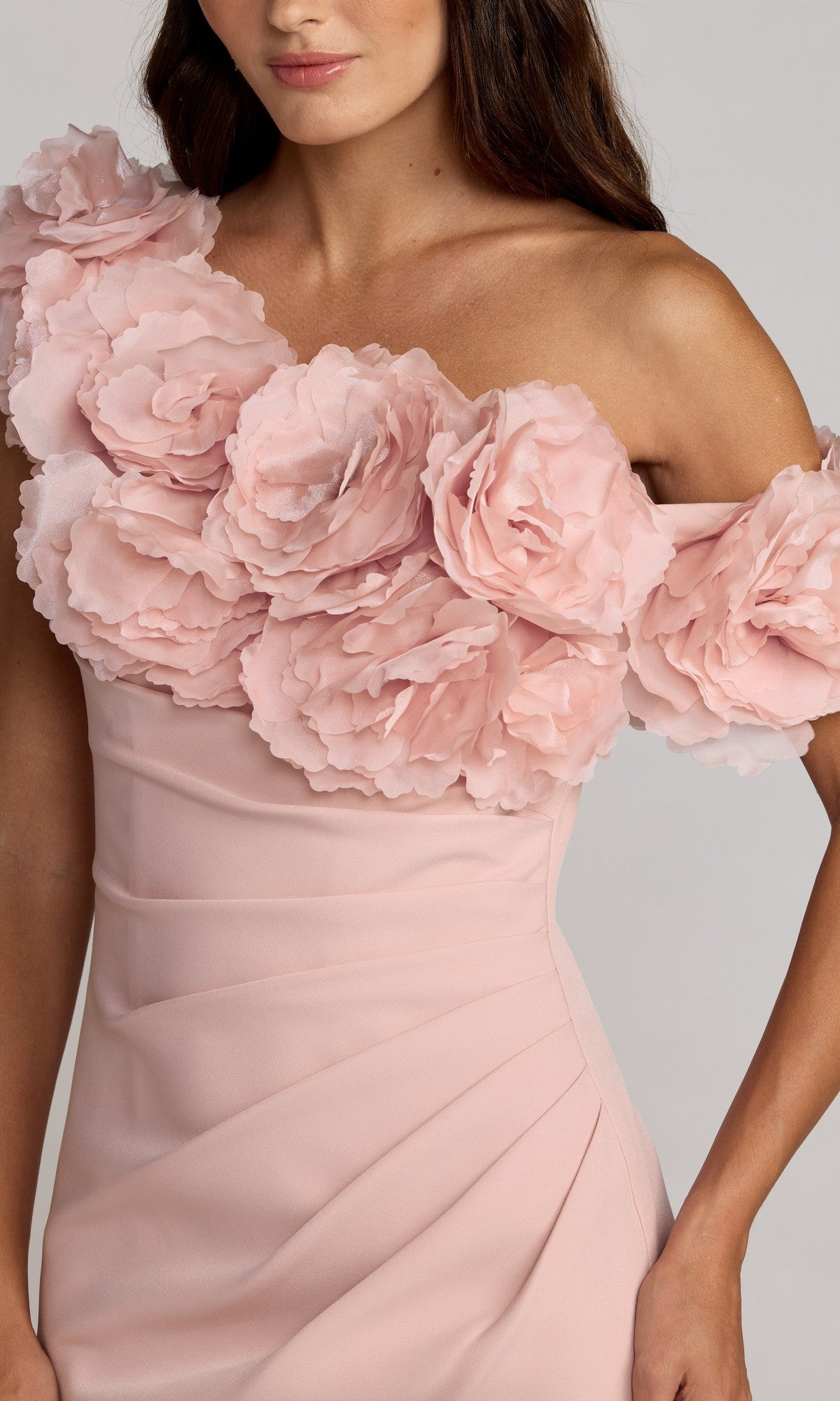 A woman wears the Mac Duggal 21383 long formal dress in light pink, featuring an off-shoulder design adorned with large, layered 3D floral appliqué details across the neckline and upper bodice.