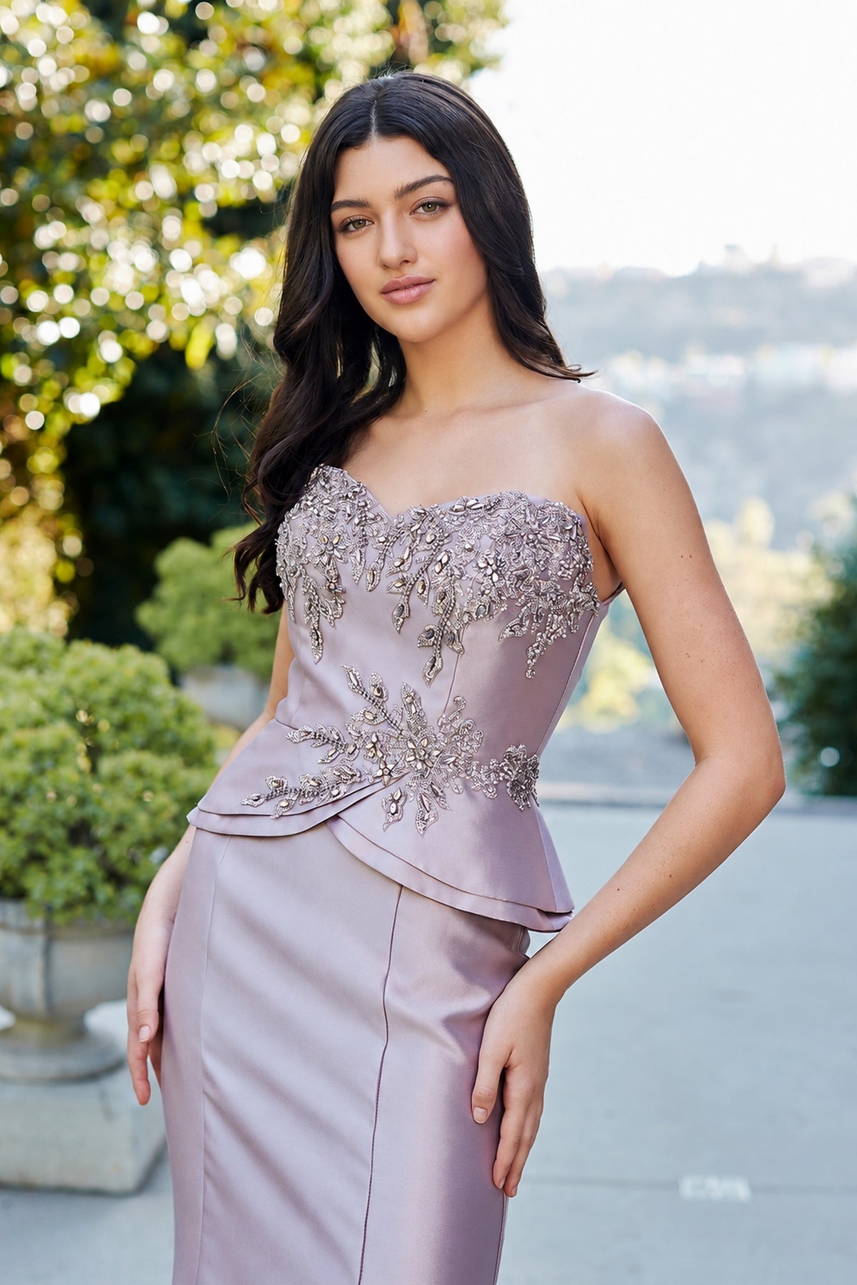 Amelia Couture 2162 is a strapless, mauve-colored evening gown with a peplum waist and floral crystal embellishments on the beaded bodice.