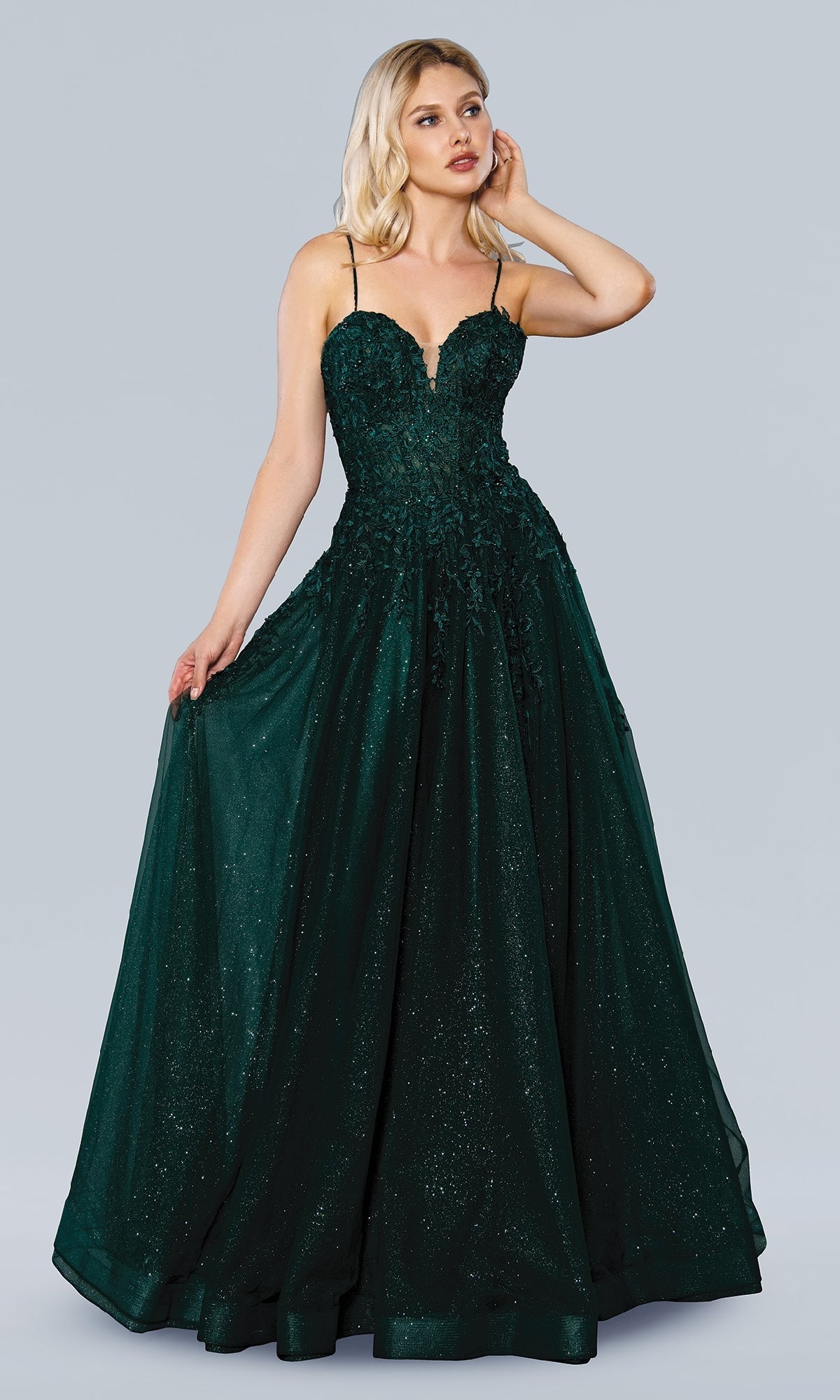 A woman poses against a plain gray background wearing the Stella Couture 22027, a dark green, floor-length sleeveless prom dress with thin straps, a lace embroidered bodice, and a full skirt.