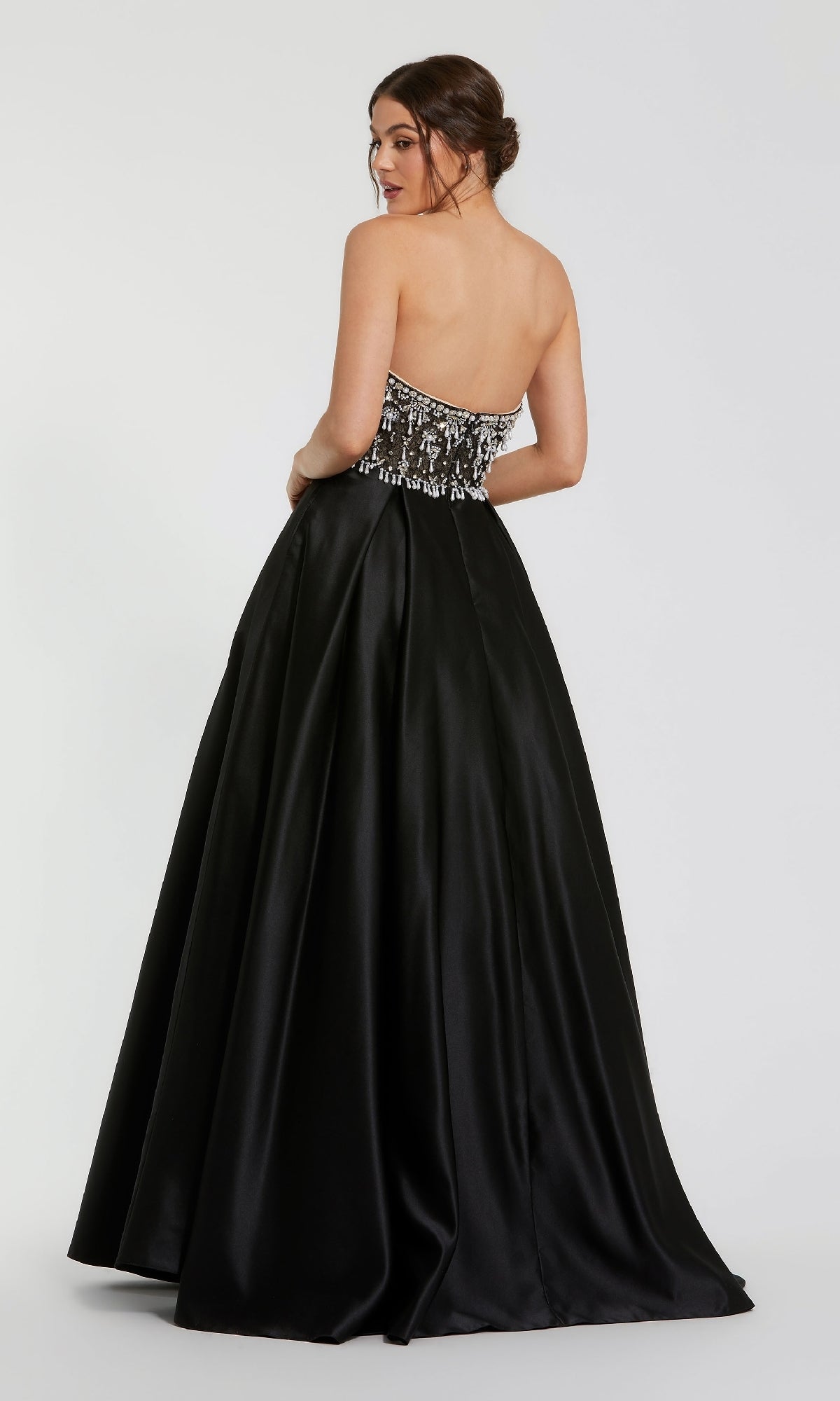 Woman models the Mac Duggal 2225 strapless black satin prom gown, featuring a beaded bodice, as she poses with her back to the camera against a plain background.