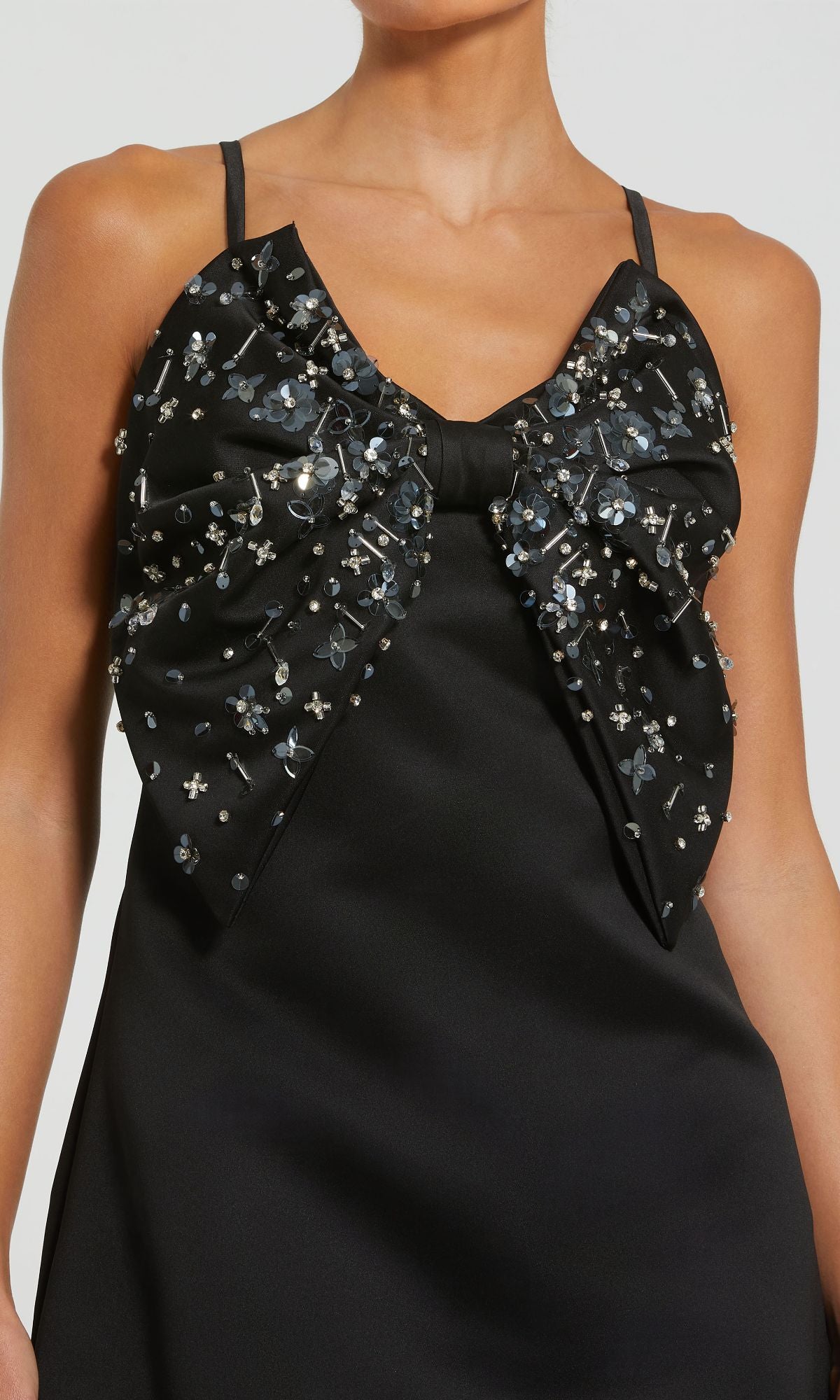 A woman wearing the Mac Duggal 2232 Black Satin Mini Cocktail Dress, featuring a large beaded bow on the chest with silver and black bead embellishments.